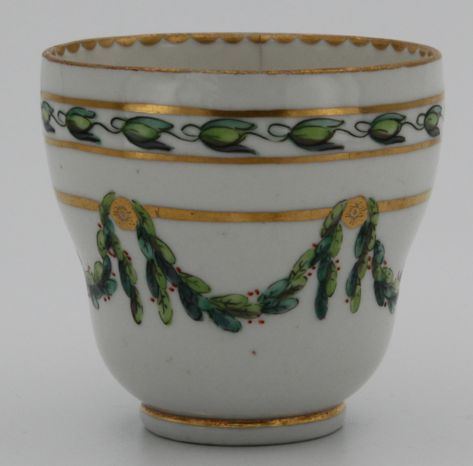 A Bristol ogee-shaped coffee cup, with harebell-moulded ear-shaped handle, painted in green and iron red with laurel swags, suspended from gilt bands within green leaf scroll bands and gilt dentil rims, circa 1775. Blue B. mark