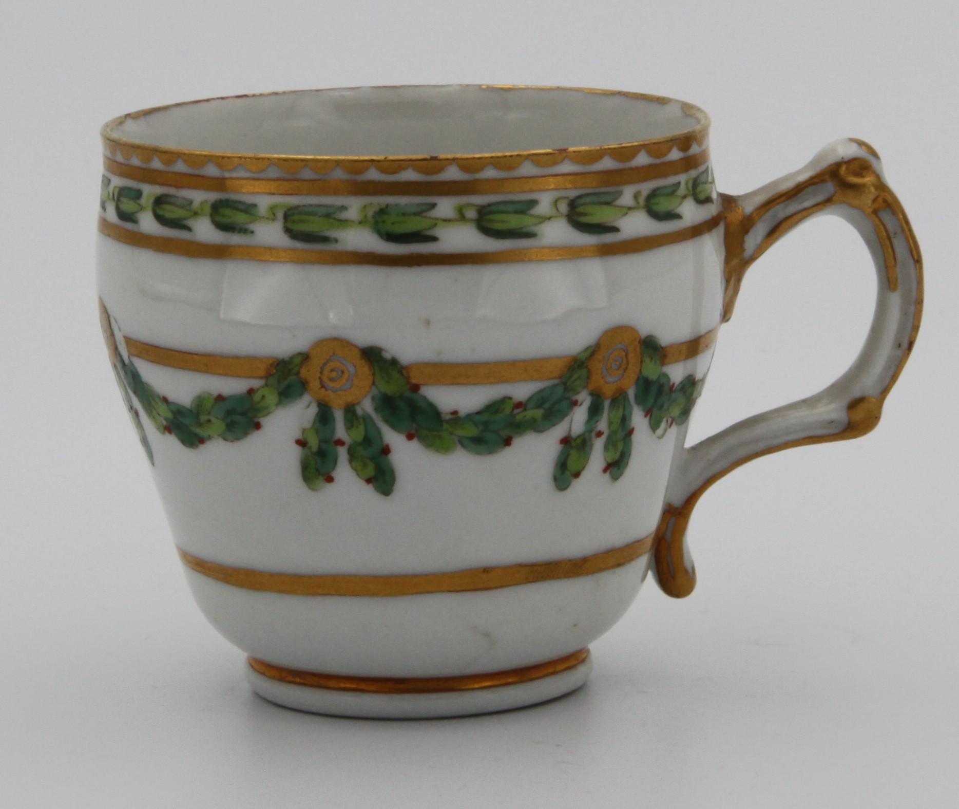 A Bristol ogee-shaped coffee cup, with harebell-moulded ear-shaped handle, painted in green and iron red with laurel swags, suspended from gilt bands within green leaf scroll bands and gilt dentil rims, circa 1775. Blue X mark