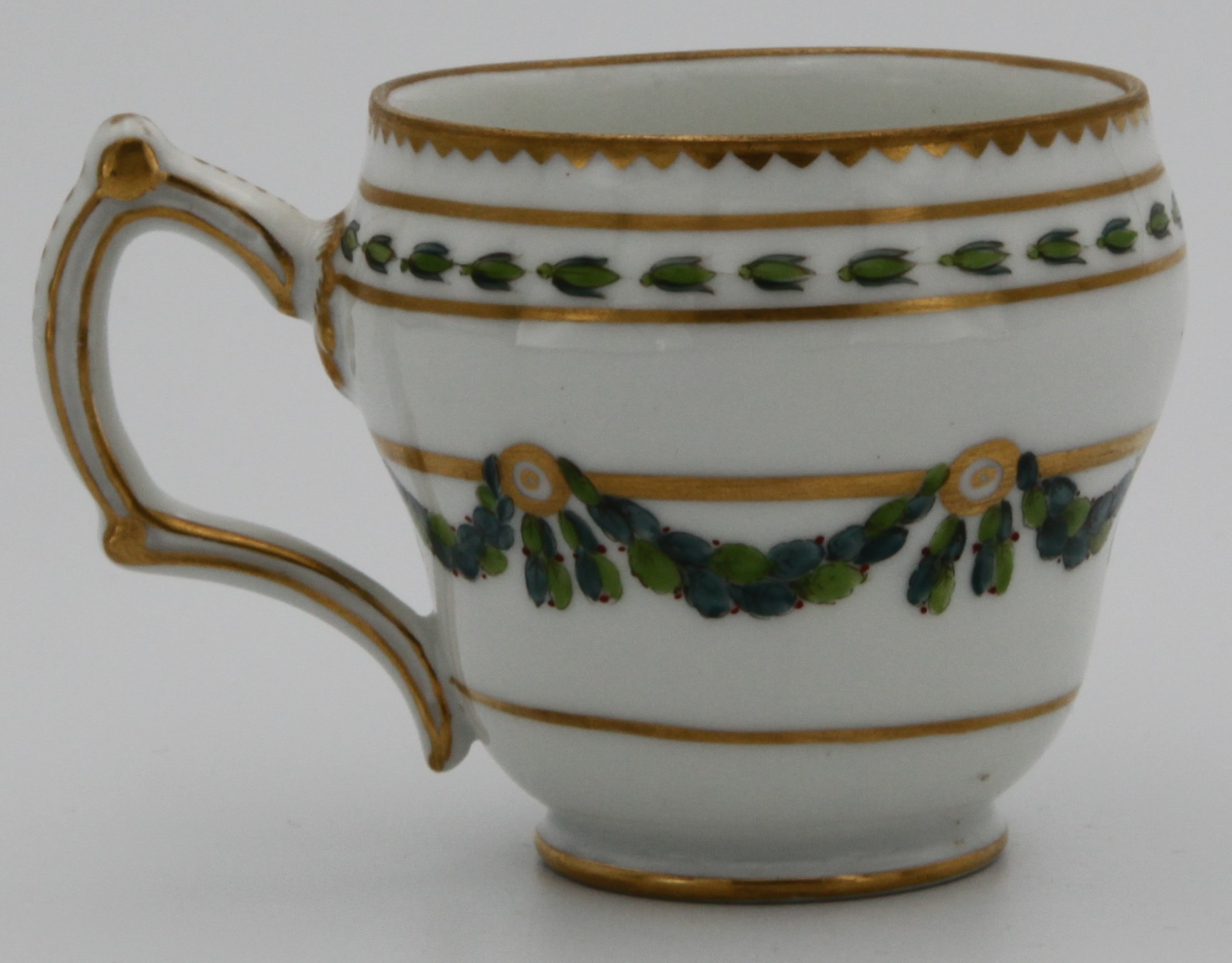 A Bristol ogee-shaped coffee cup, with harebell-moulded ear-shaped handle, painted in green and iron red with laurel swags, suspended from gilt bands within green leaf scroll bands and gilt dentil rims, circa 1775. Blue X3 mark