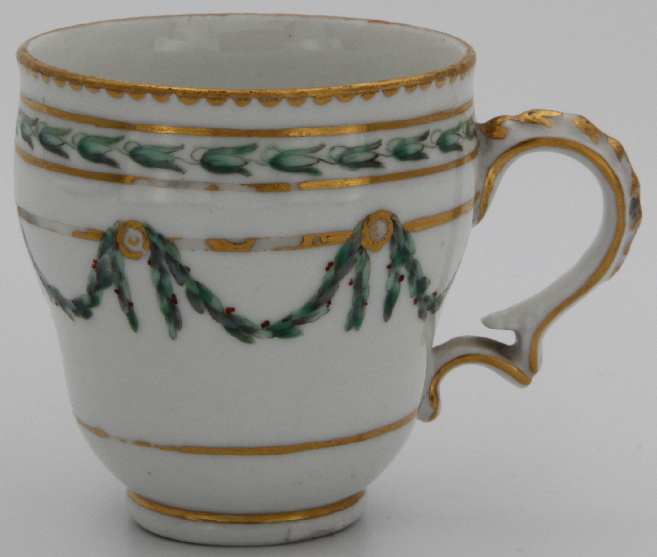 A Bristol ogee-shaped coffee cup, with harebell-moulded ear-shaped handle, painted in green and iron red with laurel swags, suspended from gilt bands within green leaf scroll bands and gilt dentil rims, circa 1775. Blue X gilt 5. mark
