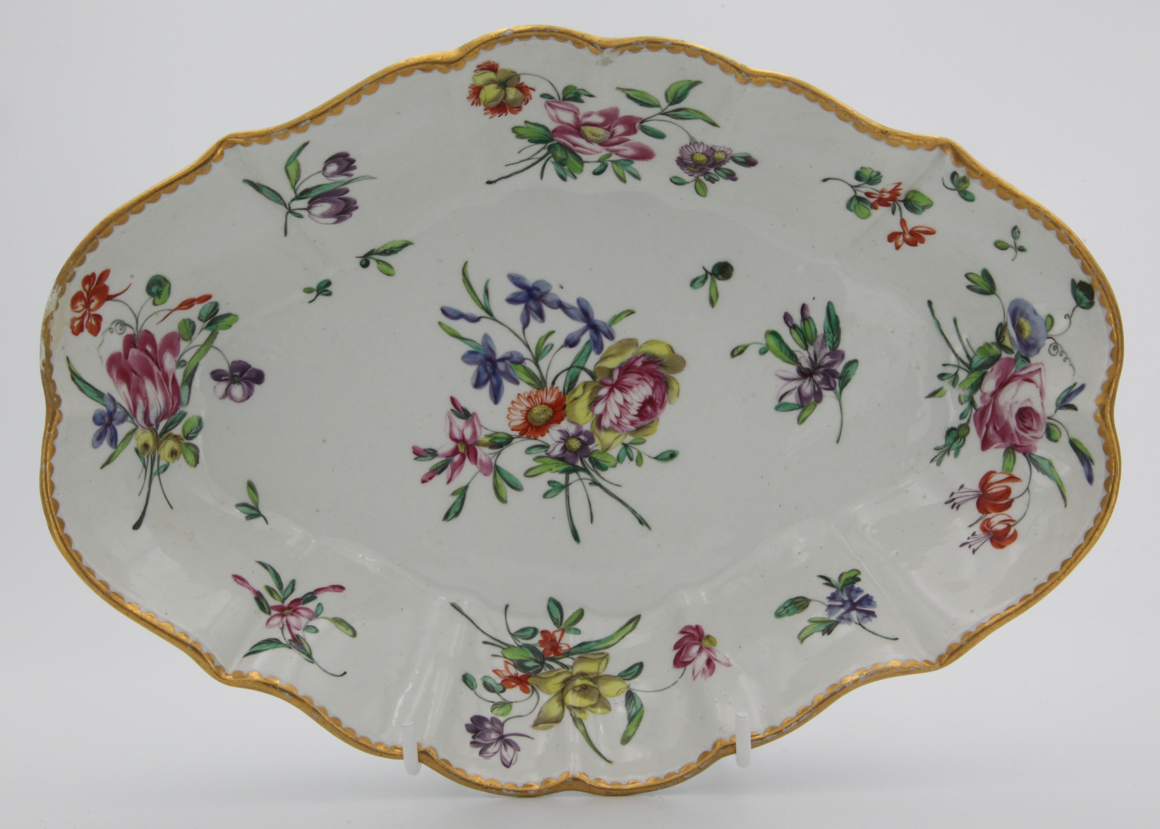 A Bristol fluted lozenge-shaped dish, painted in colourful enamels with sprays of flowers and leaves, and scattered flowers, within a gilt dentil rim,circa 1775, blue painted Xb mark.