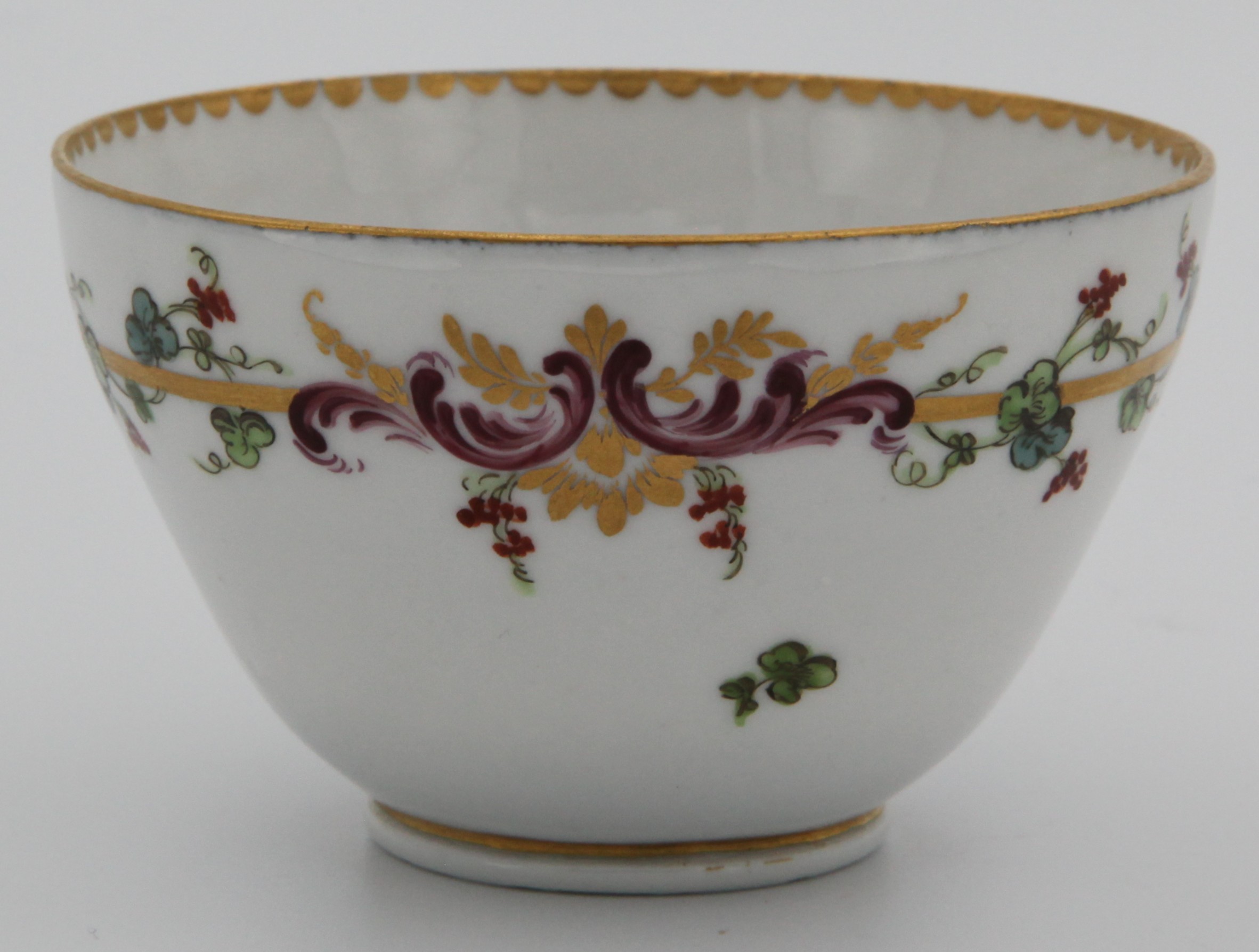 A Bristol tea bowl from the Mark Harford Service, each piece painted in purple monochrome with landscape roundels, within a gilt band, the border with iron red flowers and leaves, and puce ‘C’ scrolls, entwined with a gilt band, gilt dentil rims, circa 1772, no marks. .