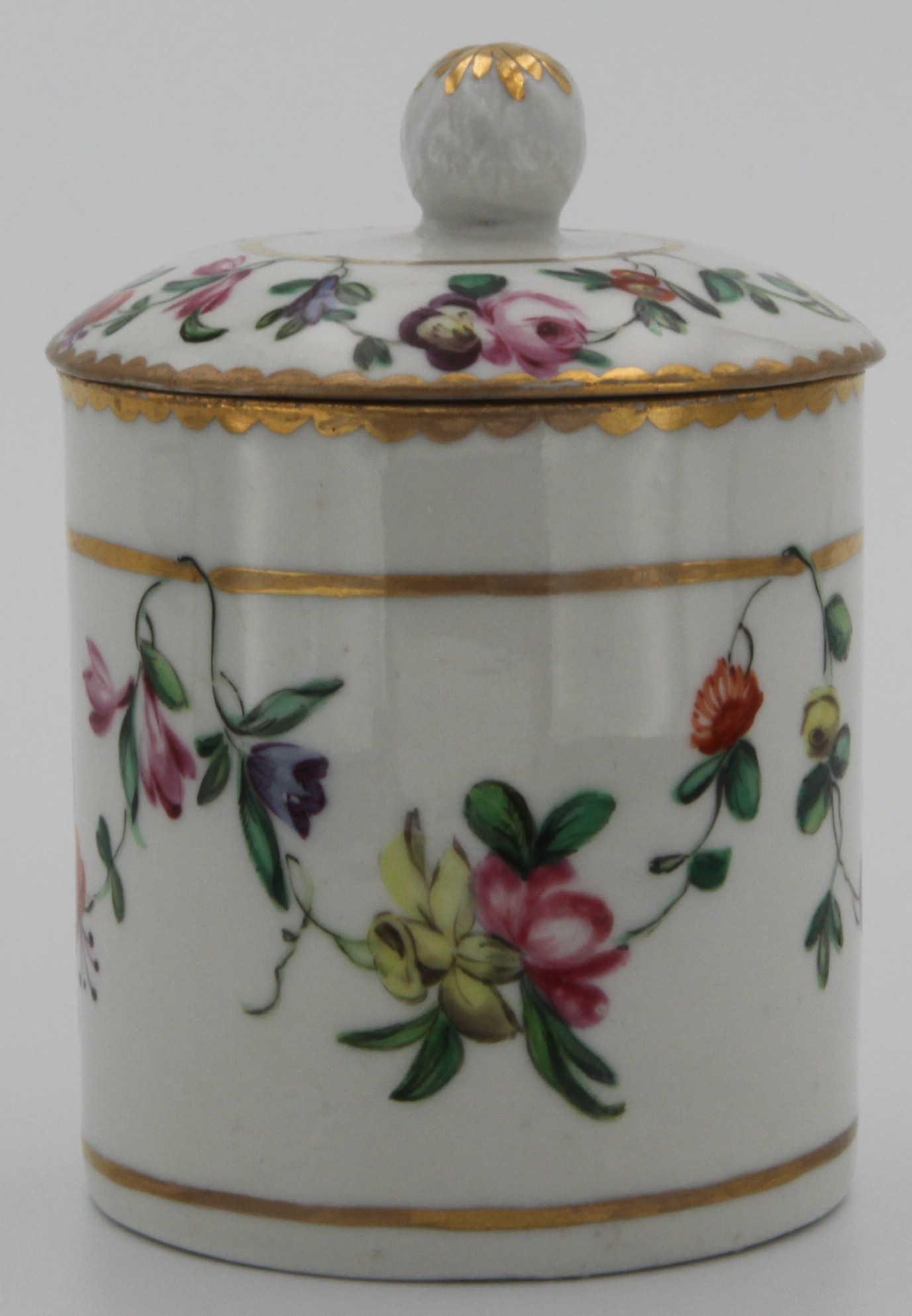 A Bristol cylindrical toilet pot and cover, with fruit knop, painted in coloured enamels with swags of flowers and leaves, suspended from gilt bands, within gilt dentil borders, circa 1772-75, blue X mark.