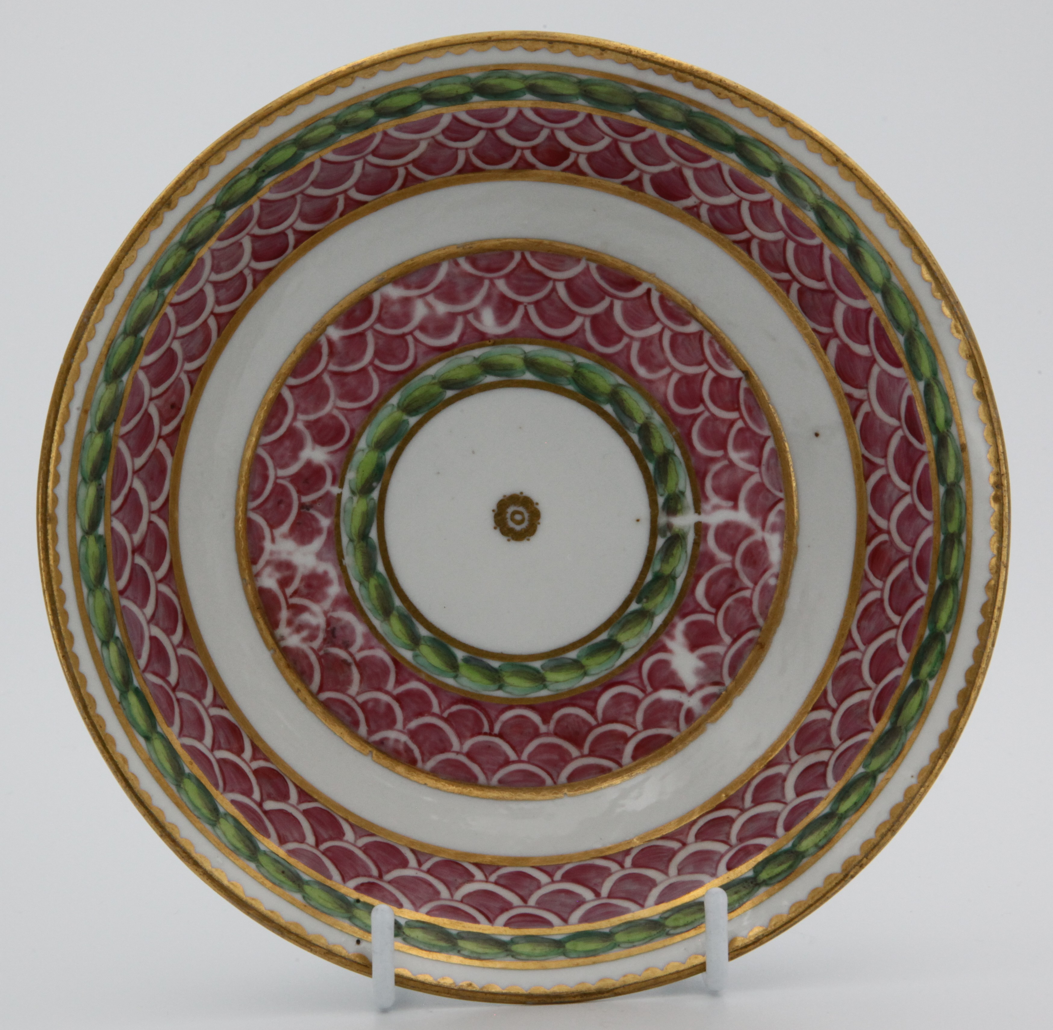 A fine Bristol coffee saucer, painted in pink with scale bands, within green laurel borders, gilt dentil rims, circa 1775, blue painted  X4 on saucer.  See Albert Amor Limited, The Alfred Trapnell Collection, 1912, numbers 27 and 28 for similar examples