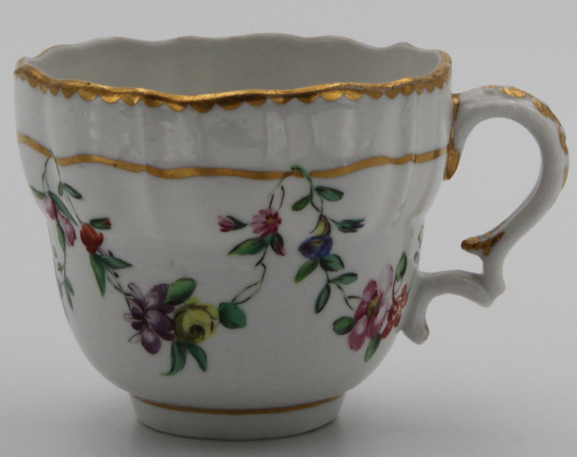 A Bristol ogee shaped coffee cup  with harebell moulded scroll handle, painted in coloured enamels with swags of flowers and leaves, suspended from gilt bands, gilt dentil borders, circa 1775, blue painted X and numeral 5 mark