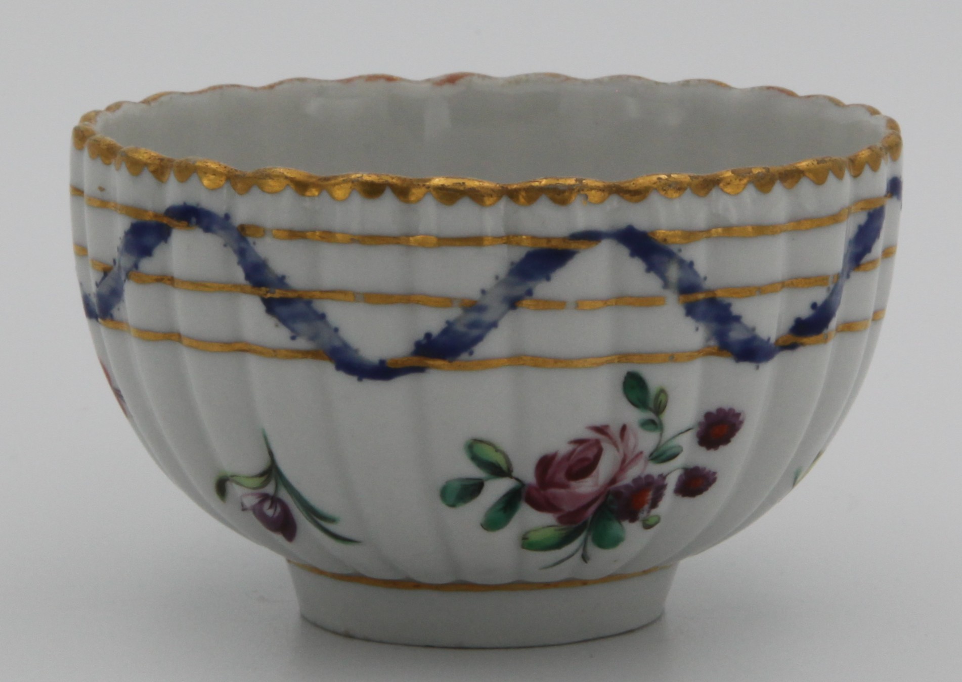 A Bristol ‘Nelson Pattern’ fluted teacup with harebell moulded scroll handle, painted in coloured enamels with scattered flowers and leaves, within scrolling blue ribbons, entwined with three gilt bands, gilt dentil rims, circa 1772, blue painted X mark and numeral 5. See Albert Amor, The Trapnell Collection, 1912, numbers 182-189, for pieces from this service, owned by Admiral Lord Nelson, and by descent to Hilaire, Countess Nelson. It was then in the Firbank Collection