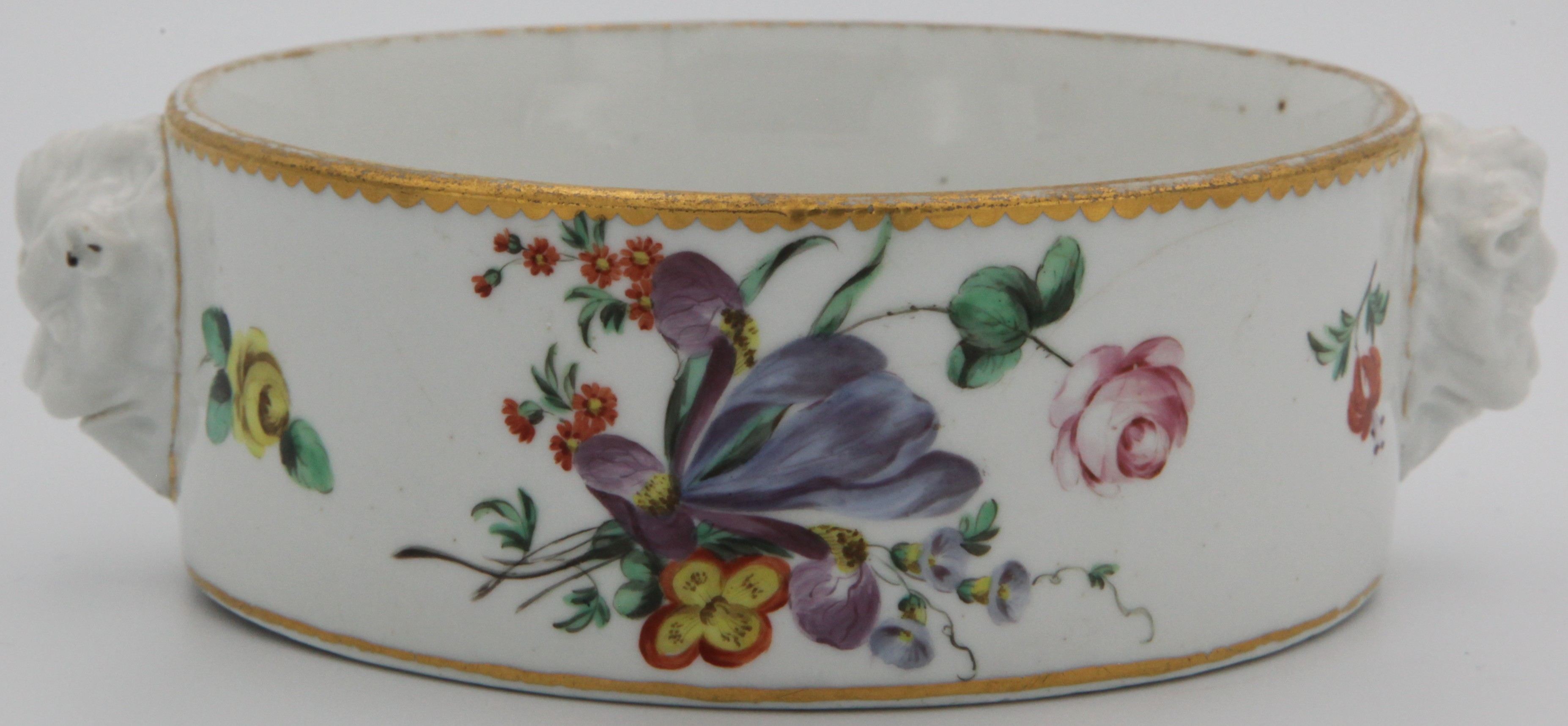 A very rare Bristol cylindrical bottle coaster, with two lion-mask-moulded handles, finely painted in coloured enamels with two sprays of flowers and leaves, and scattered flowers, within gilt line and dentil borders, circa 1775, blue painted X mark and numeral 10.  We only record one other of these coasters, photographed in the Albert Amor archive, which was sold to Peter Stephens in 1962