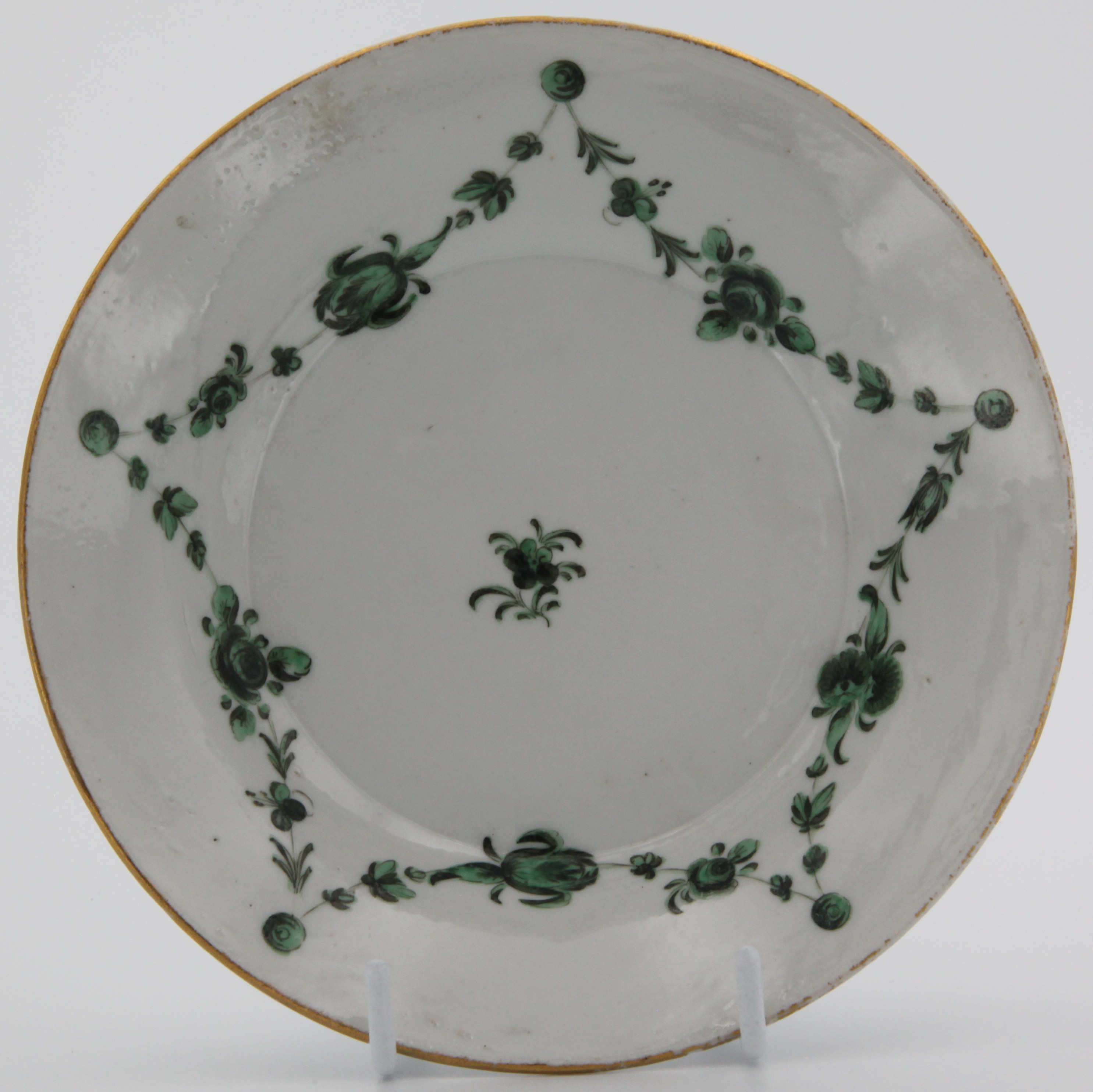 A Bristol stand, painted in green monochrome with swags of flowers and leaves, suspended from green roundels, plain gilt  border, 14.5cm across, circa 1775, grey X and 8 dot to saucer.
