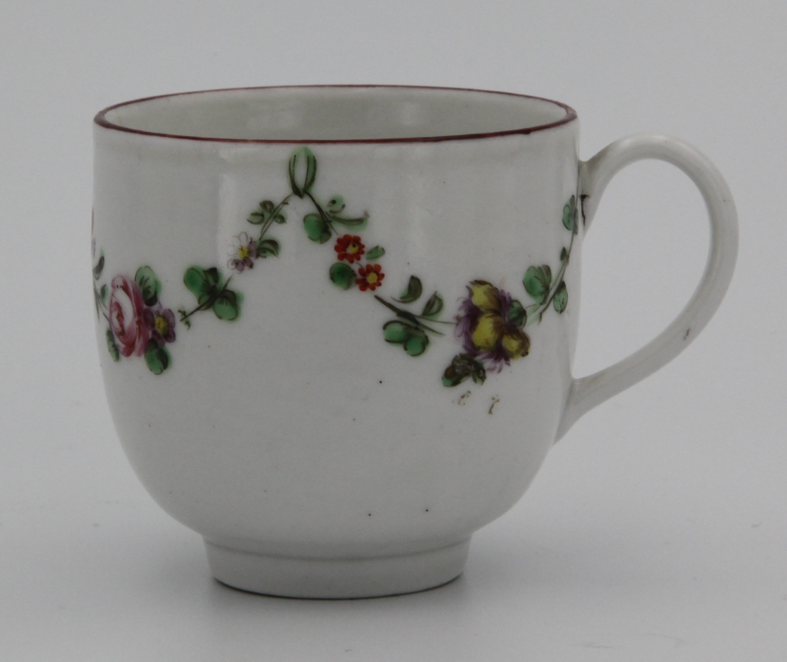 A Bristol coffee cup with simple handle, painted in enamels with garlands of flowers suspended from green loops, iron red rim, blue X16 mark