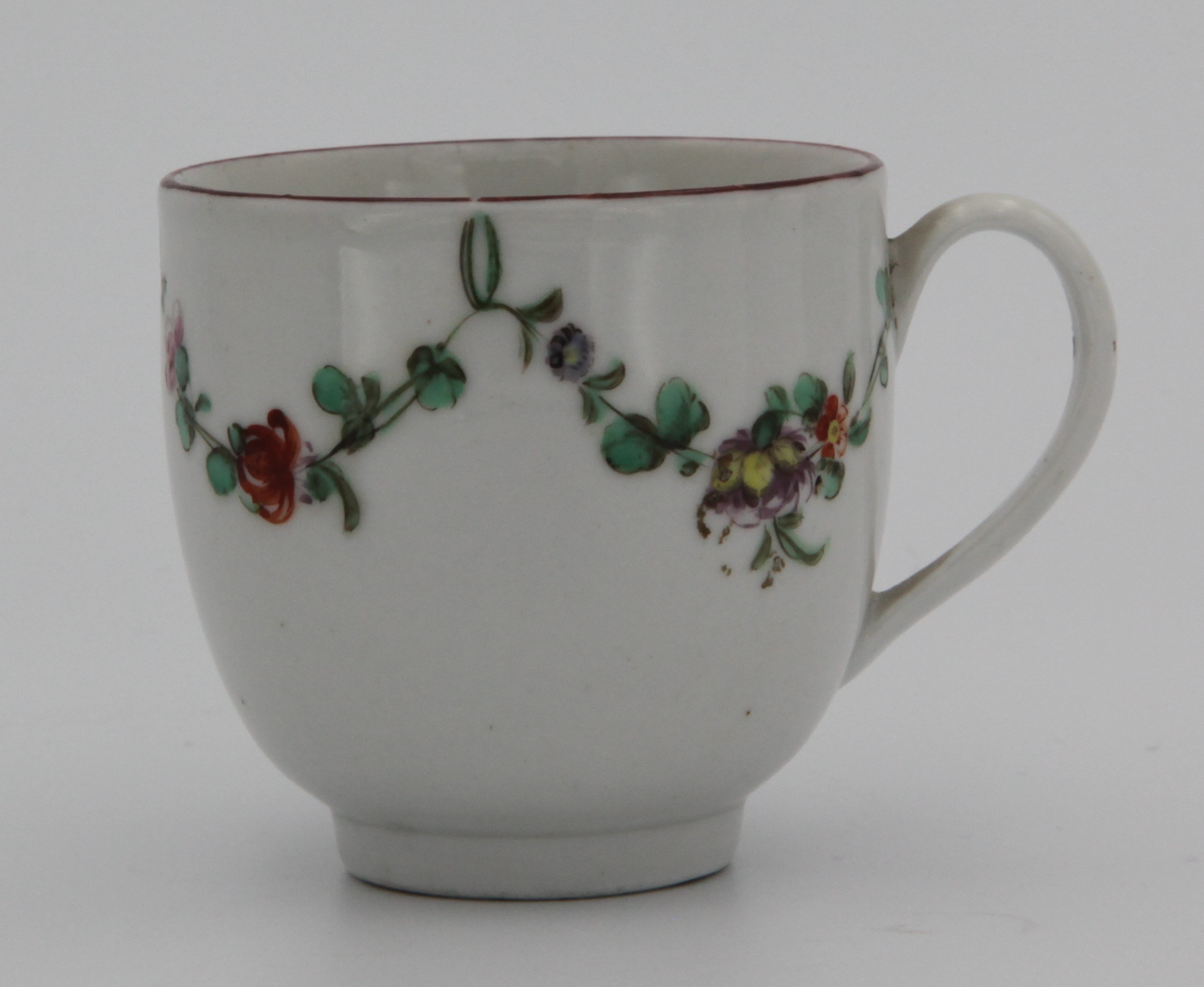 A Bristol coffee cup with simple handle, painted in enamels with garlands of flowers suspended from green loops, iron red rim, blue X16 mark