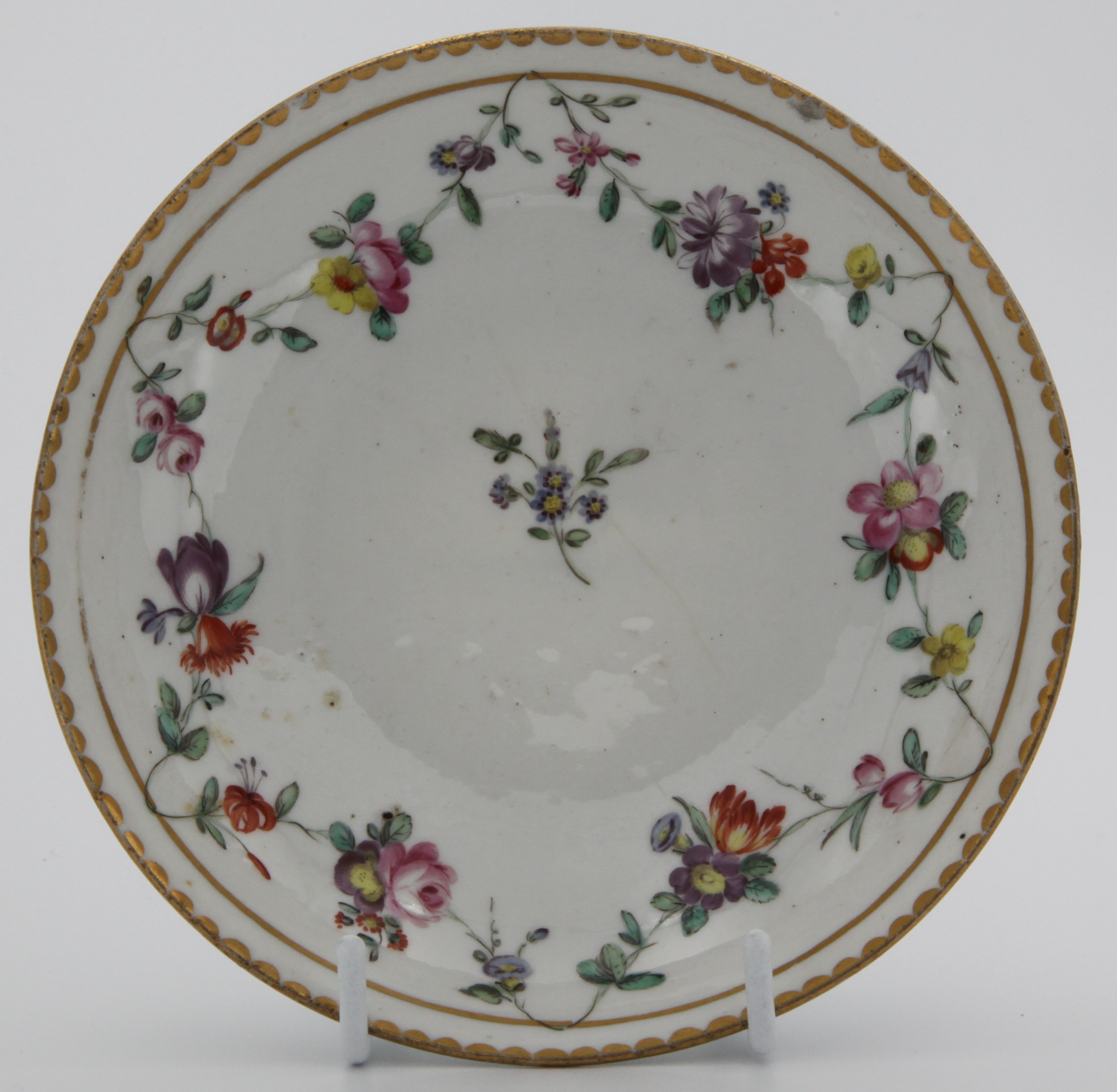 A Bristol coffee saucer painted in enamels with garlands of flowers suspended from gilt line, with gilt dentil rim, Xb mark.