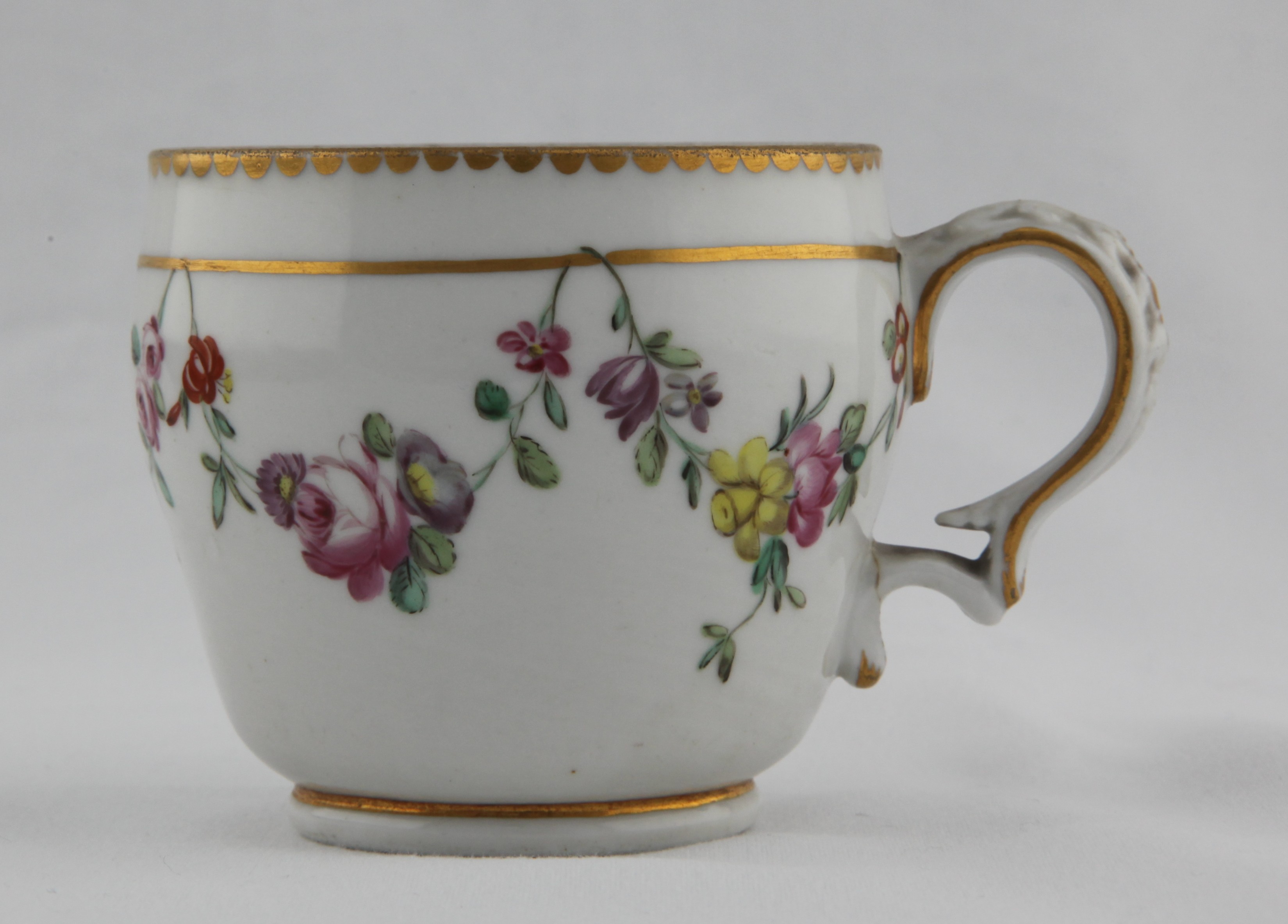 An ogee-shaped Bristol coffee cup with harebell moulded shaped handle, painted in enamels with garlands of colourful flowers suspended from gilt line, with gilt dentil rim, Xb mark