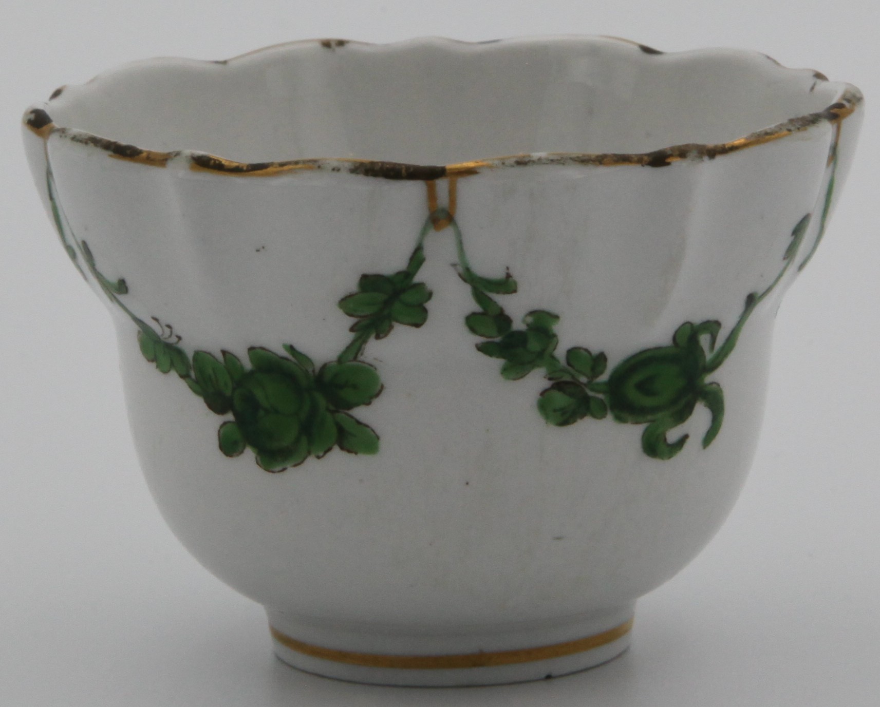 A Bristol lobed, ogee-shaped teabowl painted with green monochrome garlands of flowers and leaves suspended from gilt loops on gilt rim. No mark