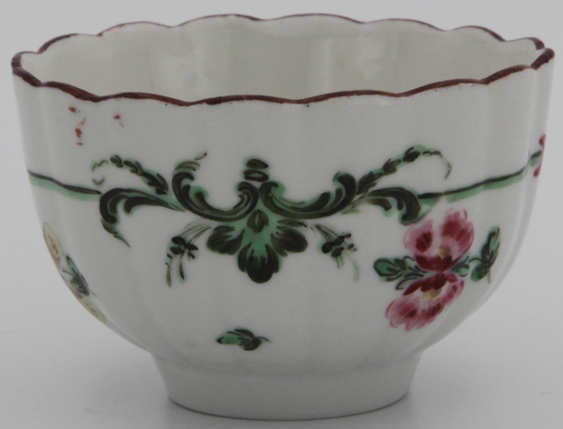 A Bristol fluted teabowl painted with green and black band with red ribbons surrounding scattered flowers and leaves, under an iron red rim line. blue X6. mark.