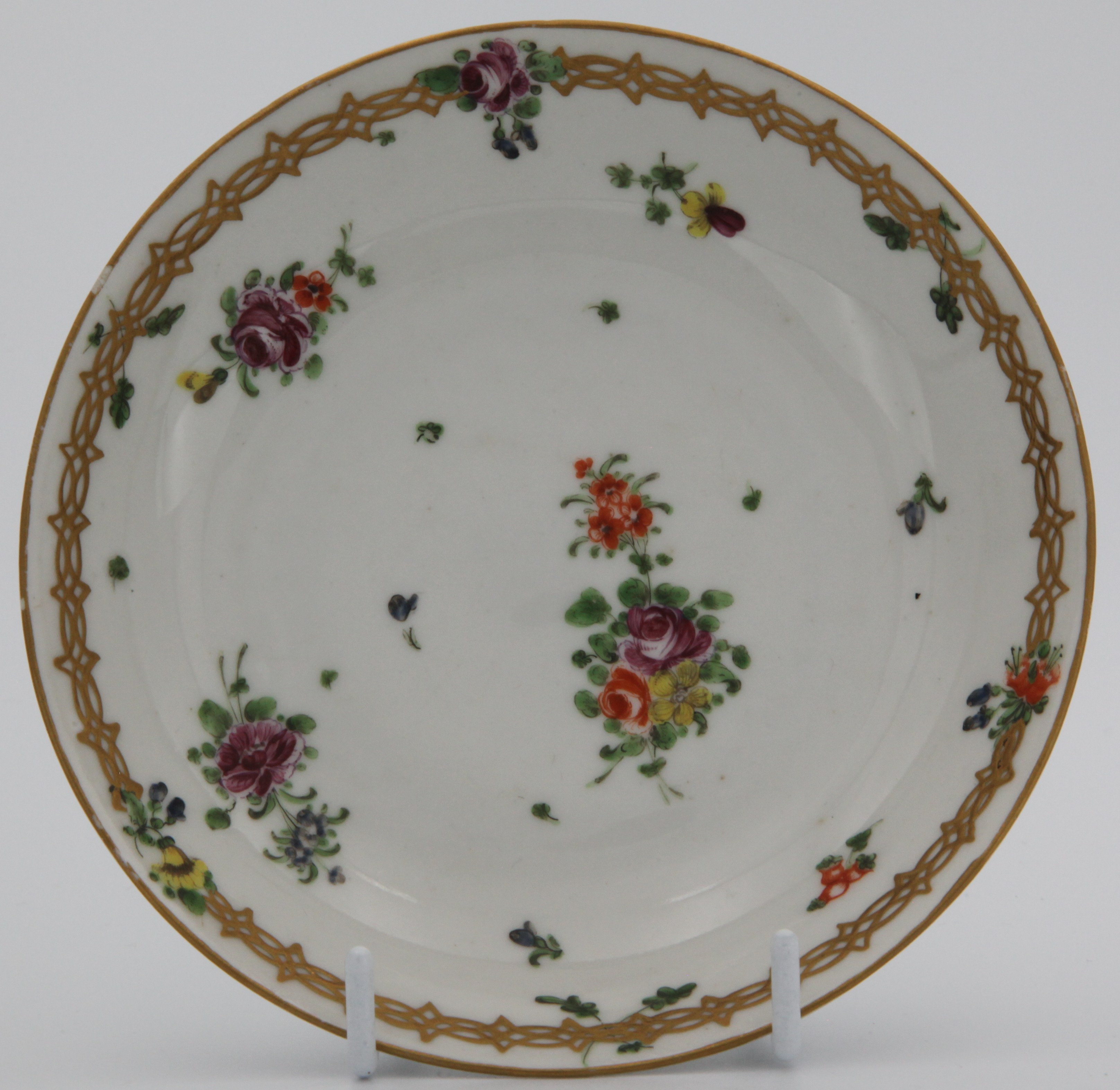 A Bristol coffee  saucer, ear-shaped gilt-painted handle, with gilt chain band (see 1247) containing leaves and flowers at the top above scattered sprays, leaves and flowers, plain gilt rims.  No mark.
