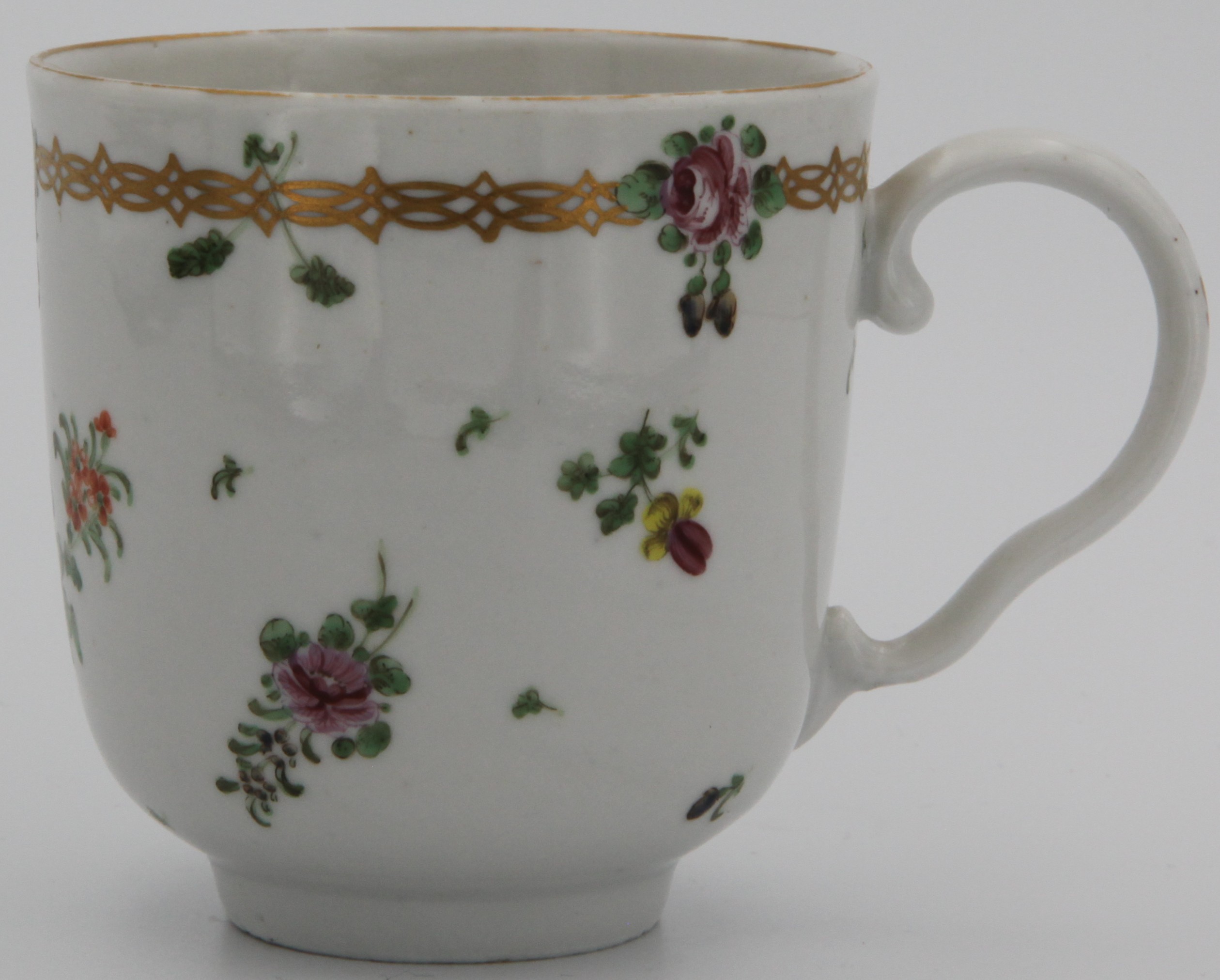 A Bristol coffee cup, ear-shaped gilt-painted handle, with gilt chain band (see 1247) containing leaves and flowers at the top above scattered sprays, leaves and flowers, plain gilt rims.  No mark