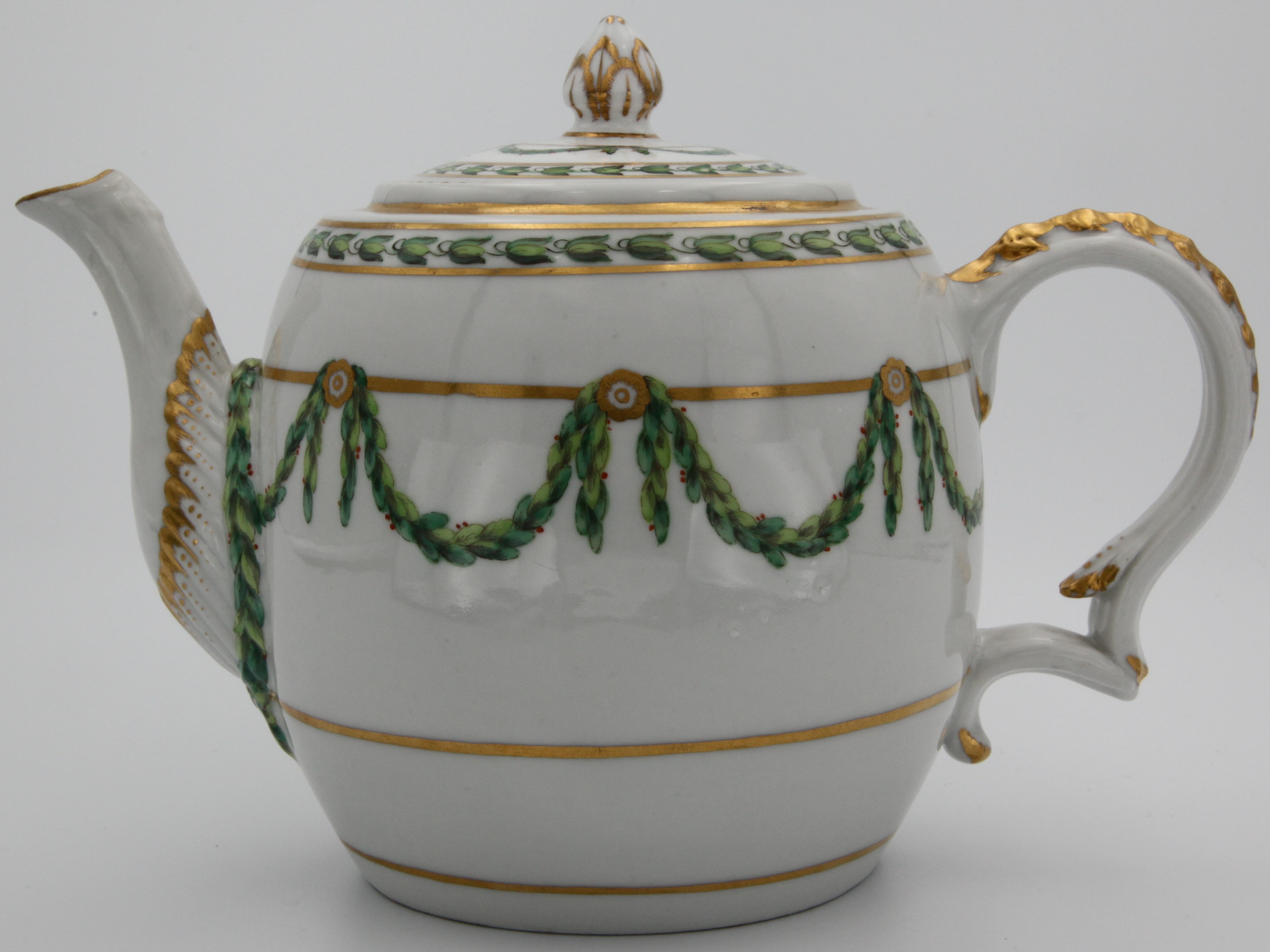 A Bristol porcelain globular teapot with cover, painted in green and iron red with laurel swags, suspended from gilt bands within green leaf scroll bands and gilt dentil rims, circa 1775. Blue X mark