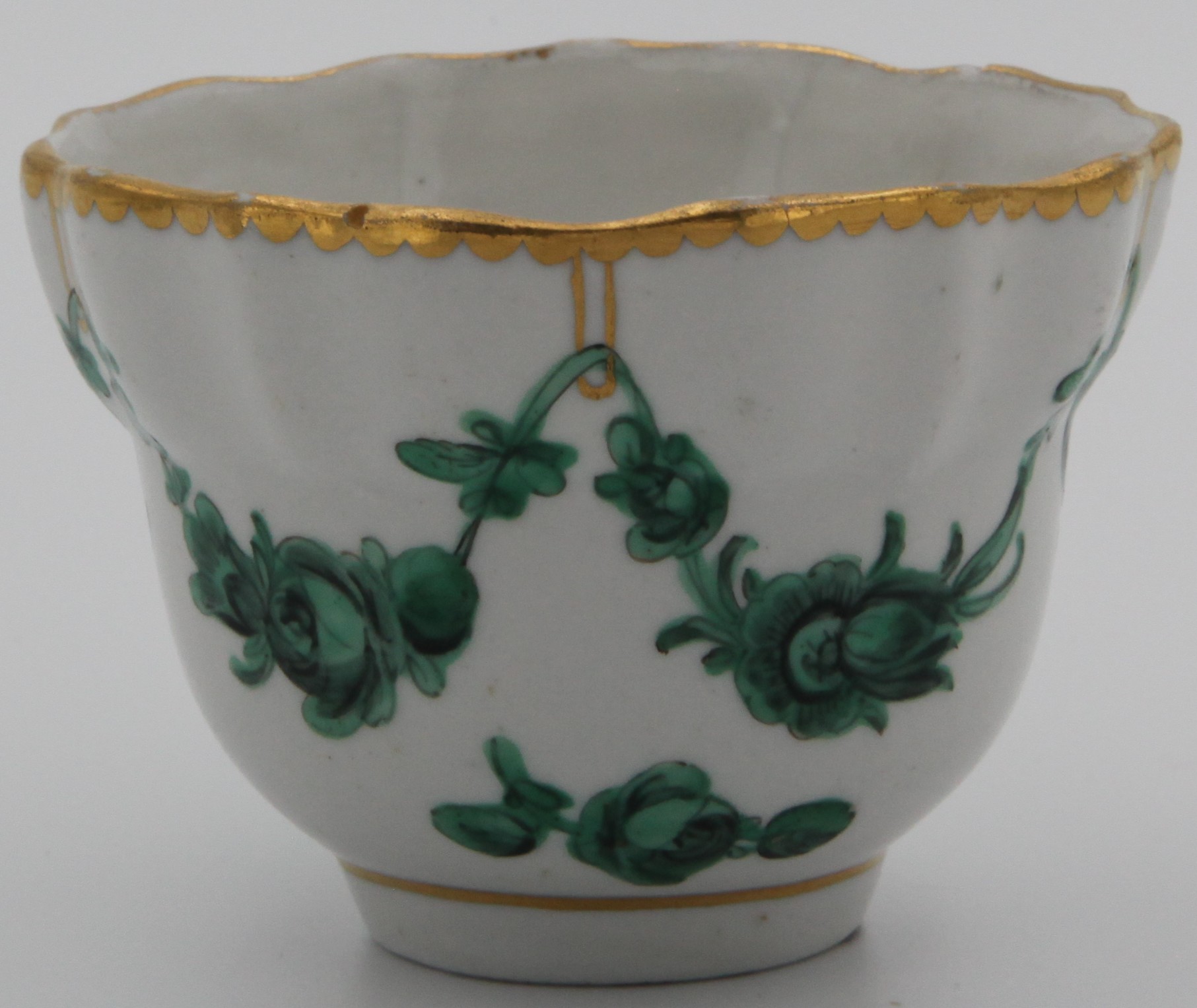 A Bristol slightly lobed ogee-shaped tea bowl, painted with green monochrome garlands suspended from gilt loops hanging from a heavy gilt dentil rim. Mark X1.