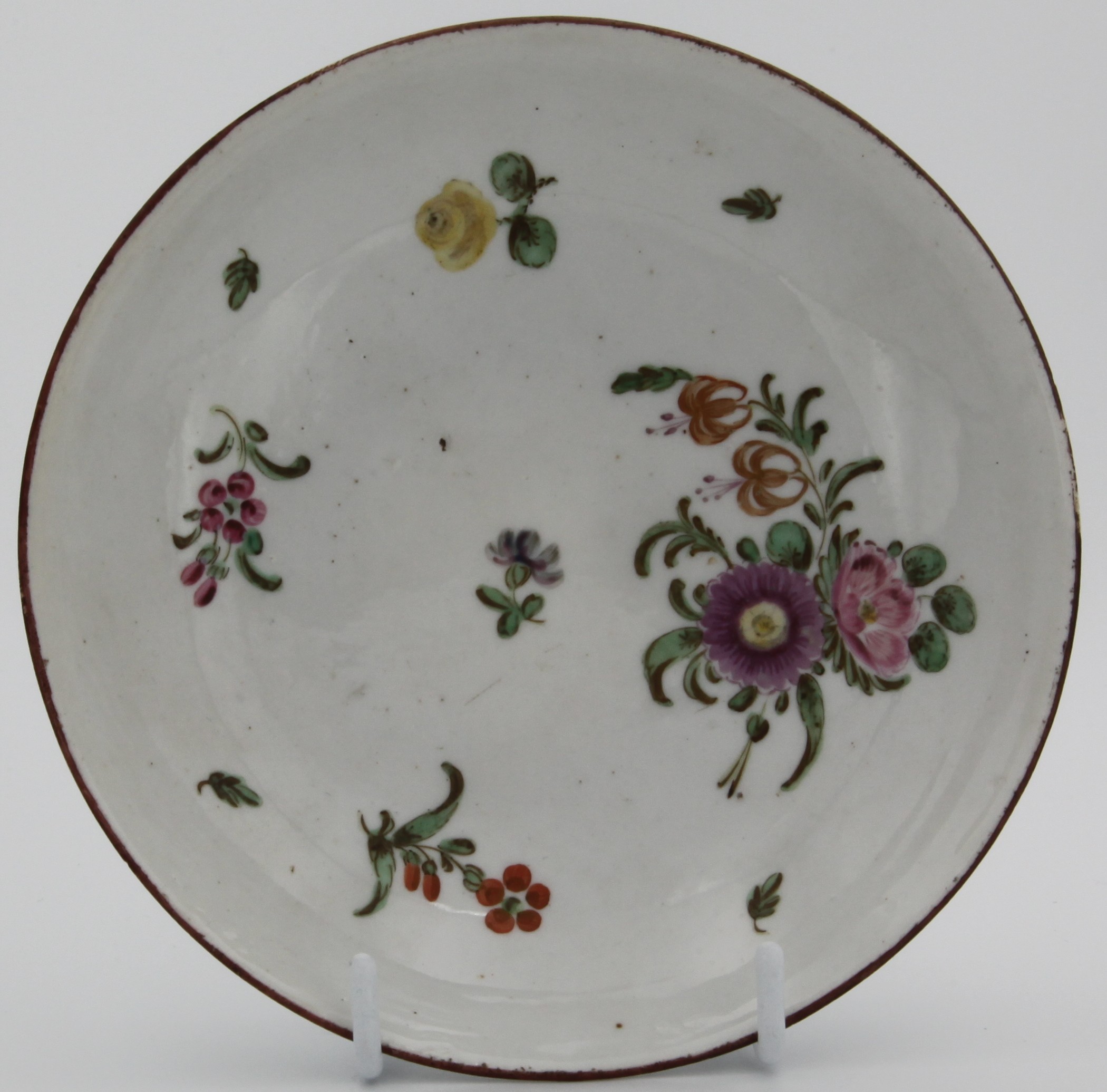 A Bristol tea saucer, circa 1775. Painted with a spray of flowers, and an iron red line rim. Blue X8. mark
