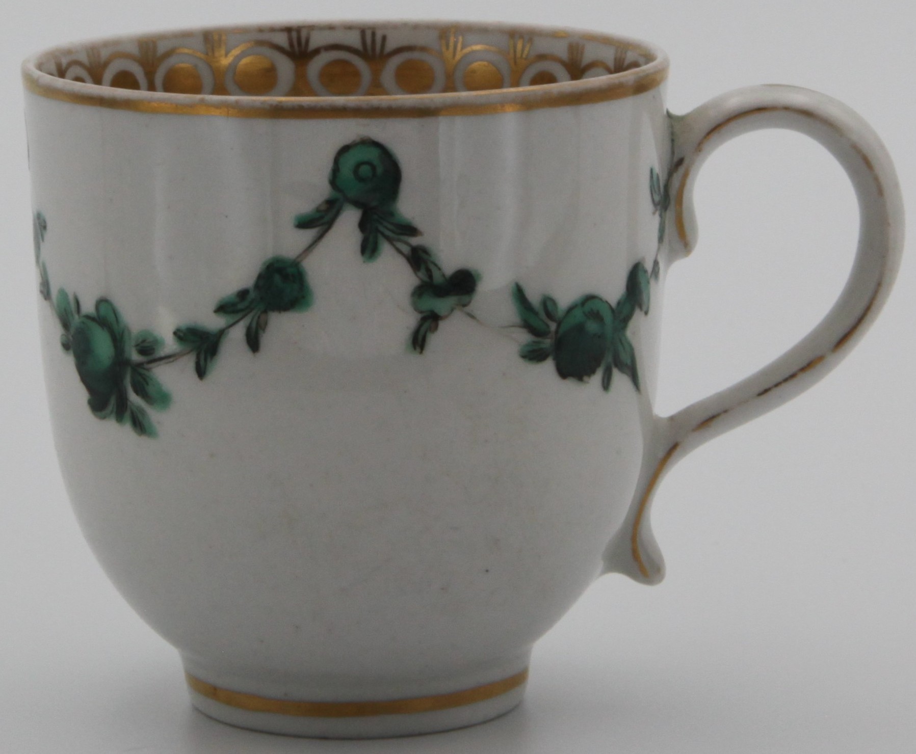 A Bristol coffee cup, painted in green monochrome with garlands of leaves and flowers suspended from roundels, gilt rim and an attractive gilt band to the inside. No mark