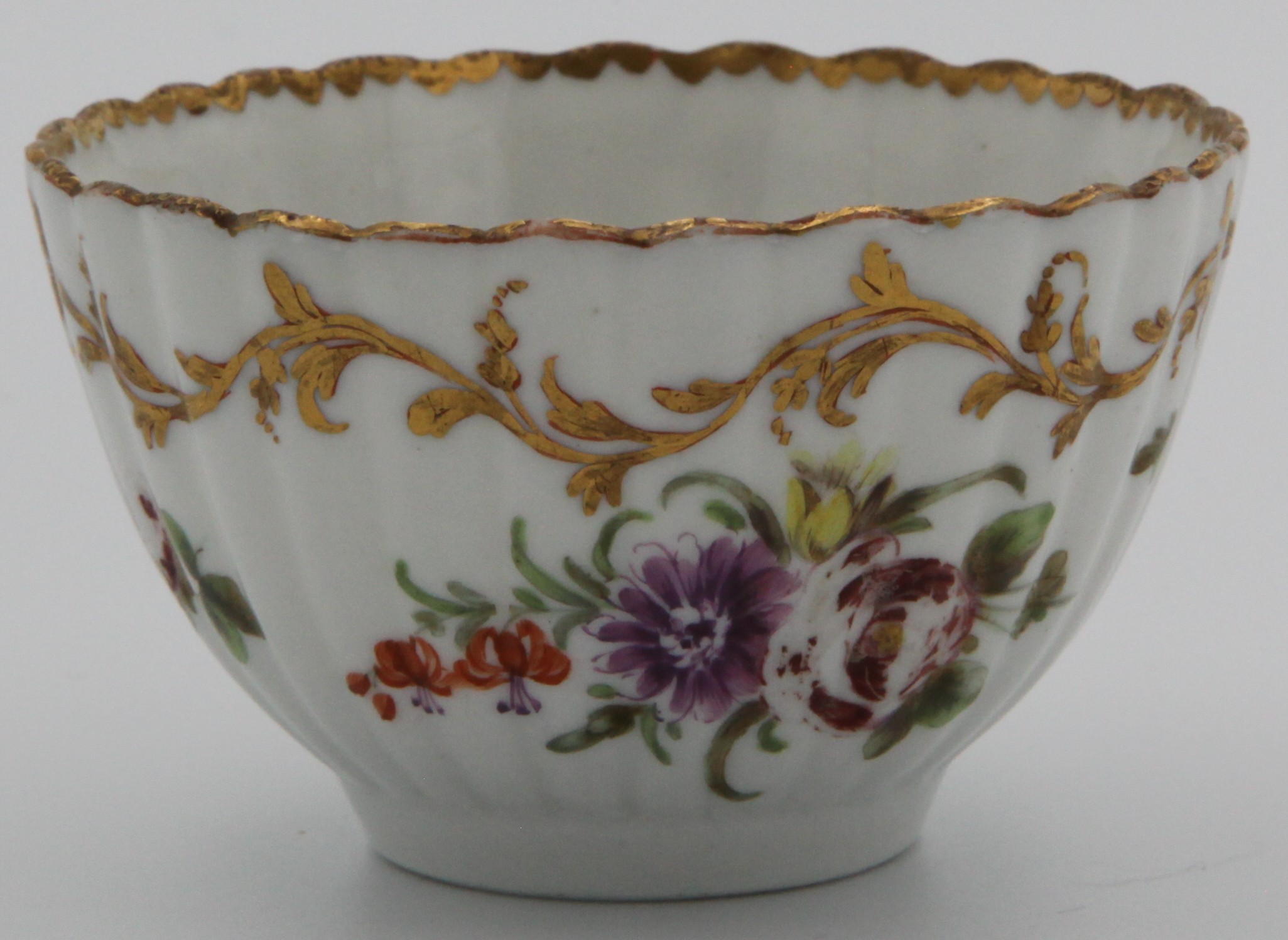 A Bristol fluted teabowl painted in colourful enamels with floral sprays and scattered sprigs, an elaborate leafy gilt scrolled border below the gilt dentil rim, blue X and gilt 1 mark. Has been matched with 1381