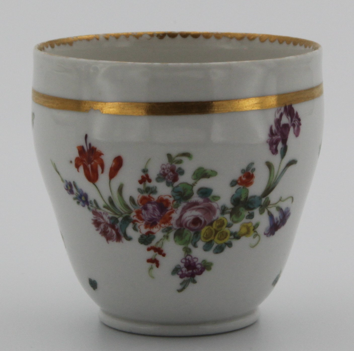 An ogee-shaped Bristol coffee cup, with angular handle, painted with floral spray and scattered flowers with prominent thick gold line under gilt dentil rim. No mark. Has been matched with 1373