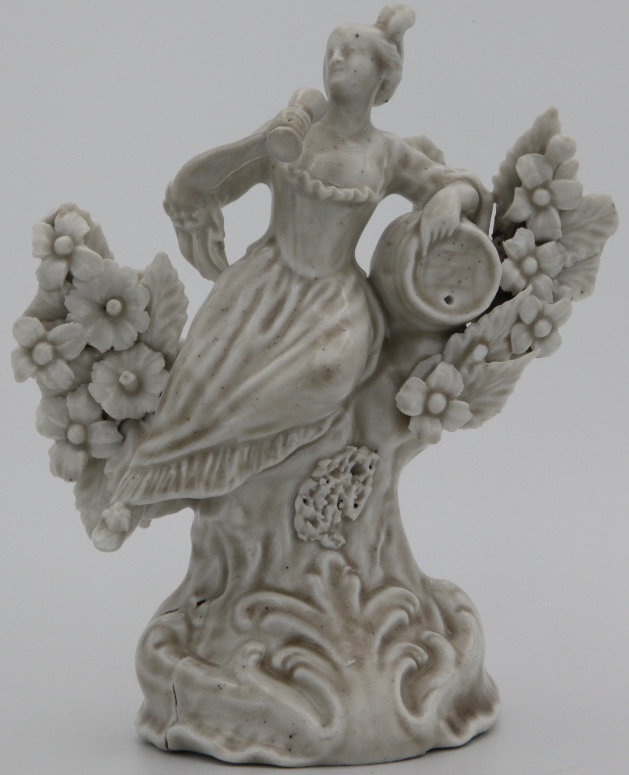 A Plymouth white-glazed figure of a female toper, c.1768-70, reclining amidst flowering bocage and leaning her left elbow on a barrel, holding a glass in her right hand, raised on a tall scrolled base. Cf. F. Severne Mackenna, Cookworthy's Plymouth & Bristol Porcelain (1946), p.81, pl.50, fig. 87.