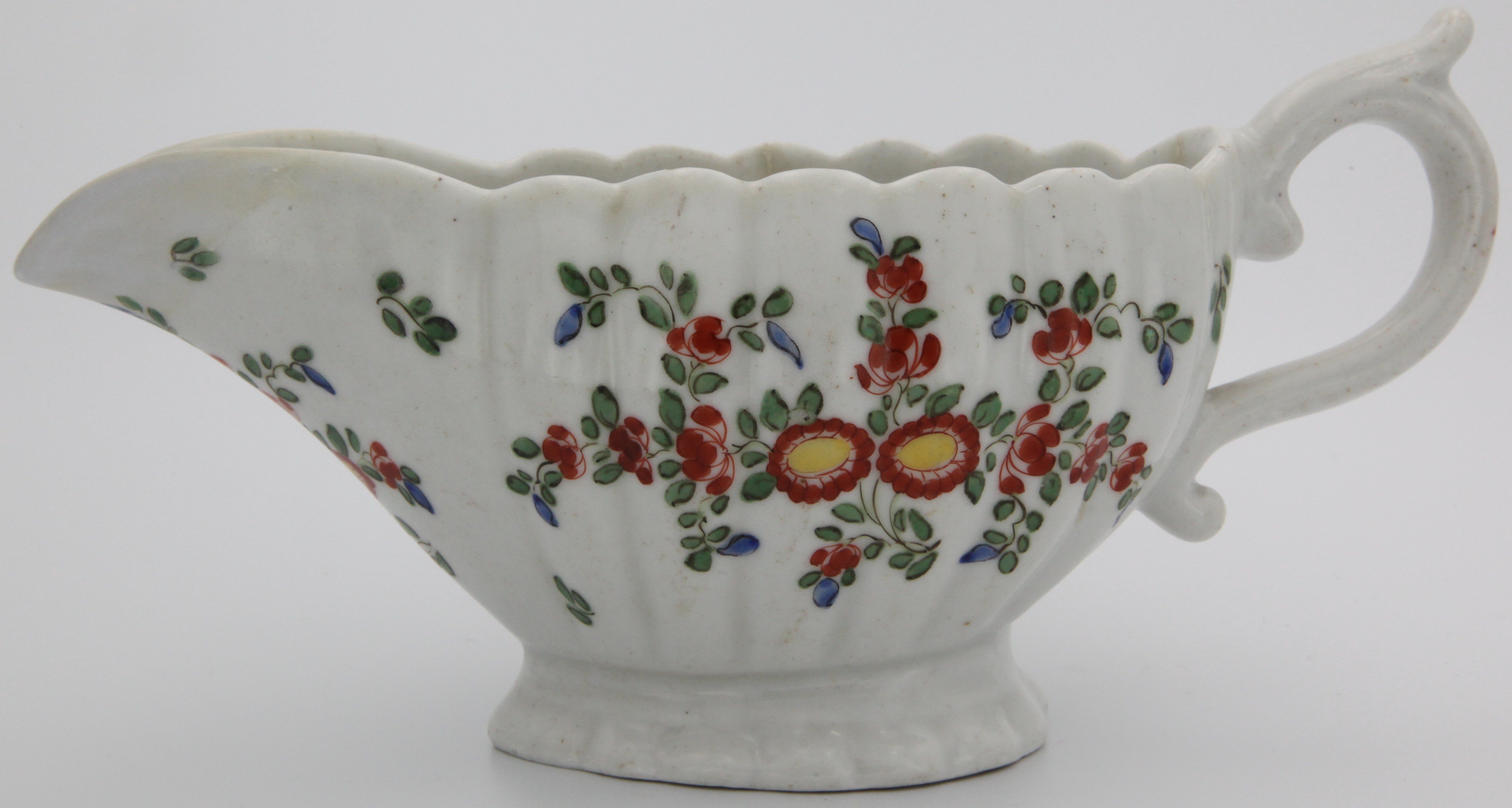 A Plymouth sauceboat with scrolling handle and thumbrest, the flute moulded body with a kakiemon style decoration of chrysanthemums, on a pedestal foot. c. 1768-70. Mark: Orange tin mark.