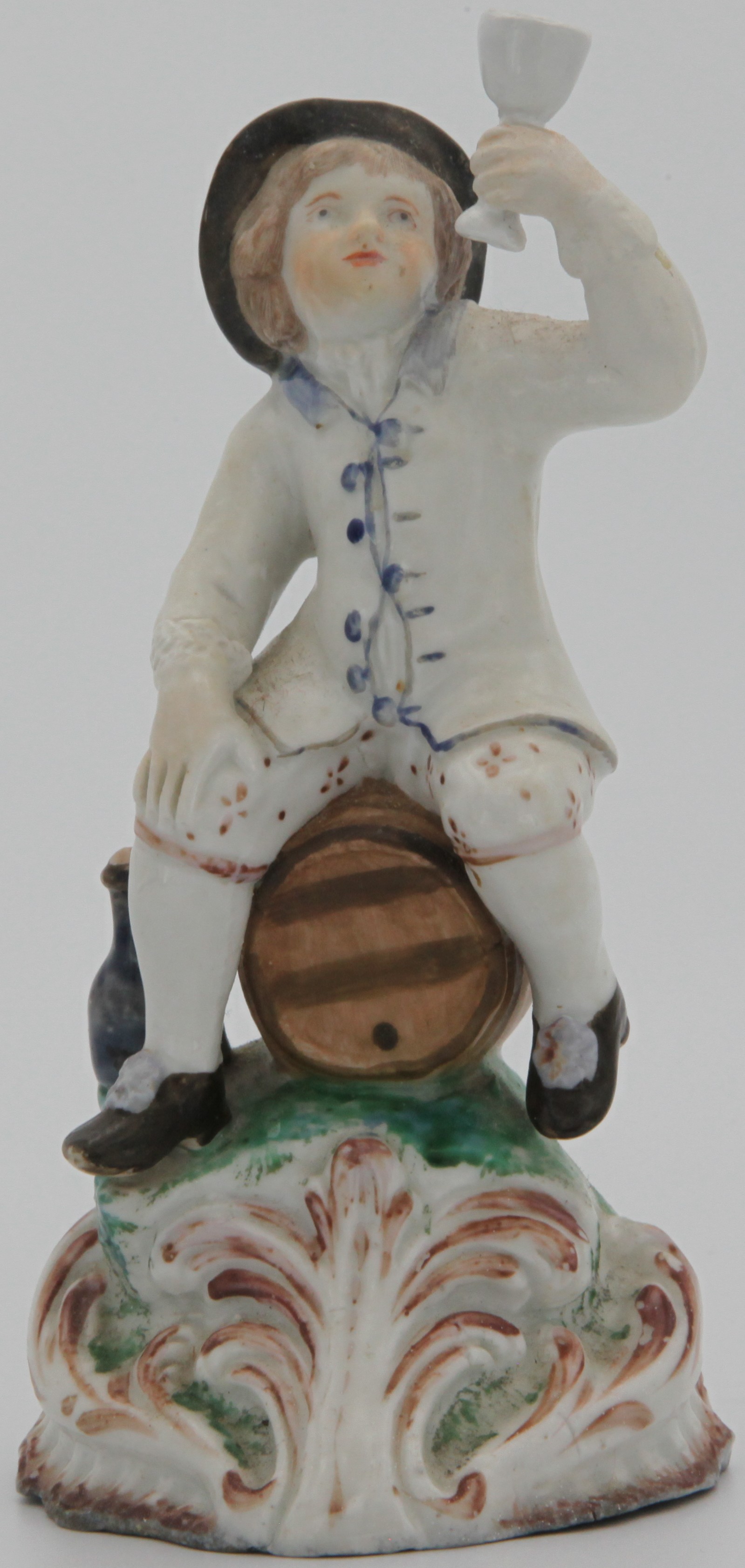 A Plymouth Toper modeled as a figure of a young boy seated astride a barrel, his left hand raised holding a cup, a bottle at his side on a scroll moulded base. c. 1768-70  Mark: none