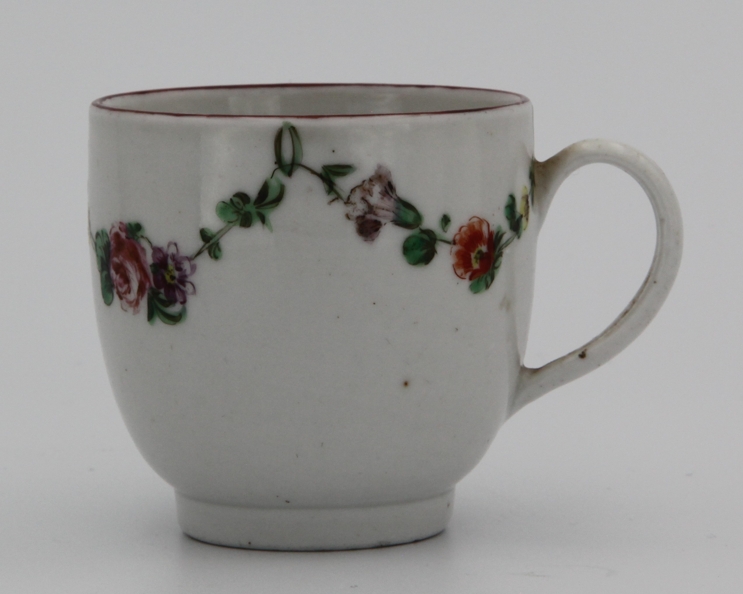 A Bristol coffee cup with simple handle, painted in enamels with garlands of flowers suspended from green loops, iron red rim, blue X16 mark