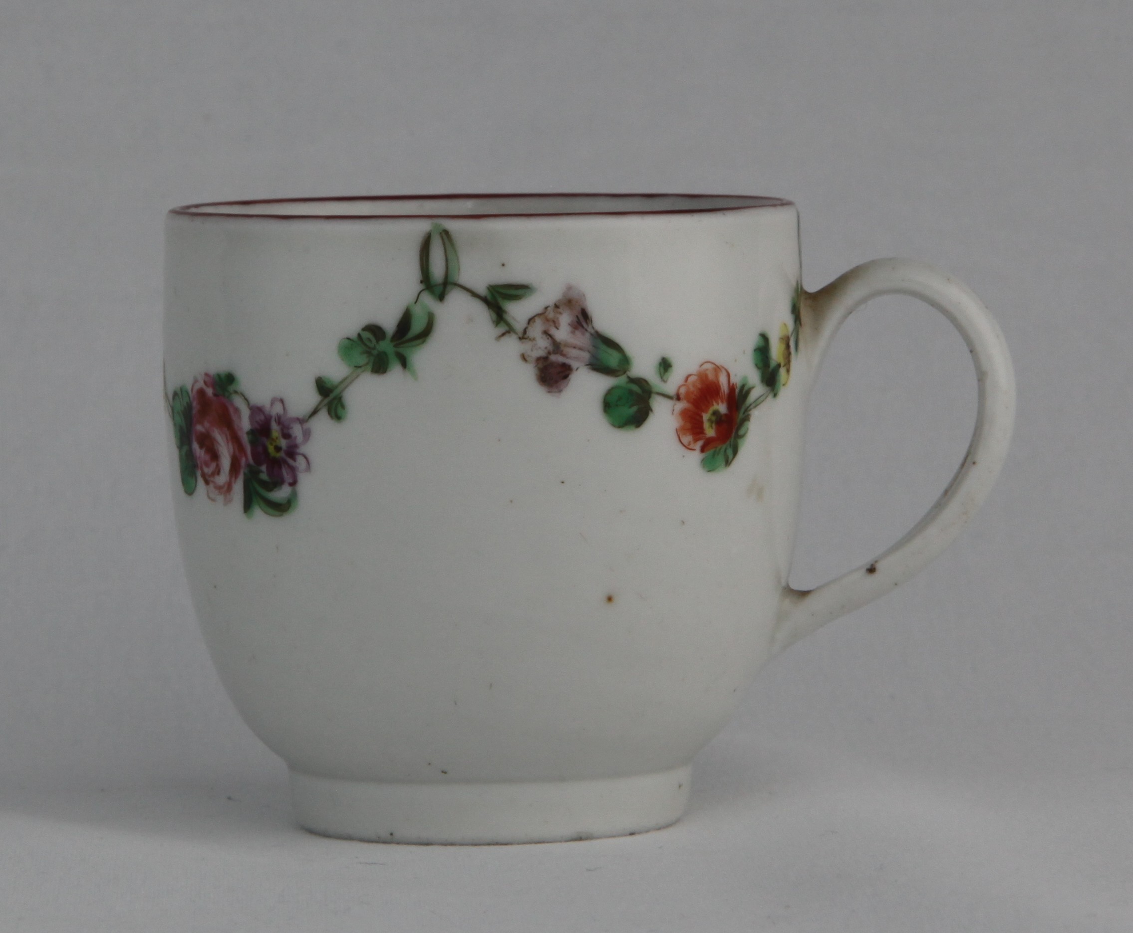 A Bristol coffee cup with simple handle, painted in enamels with garlands of flowers suspended from green loops, iron red rim, blue X16 mark