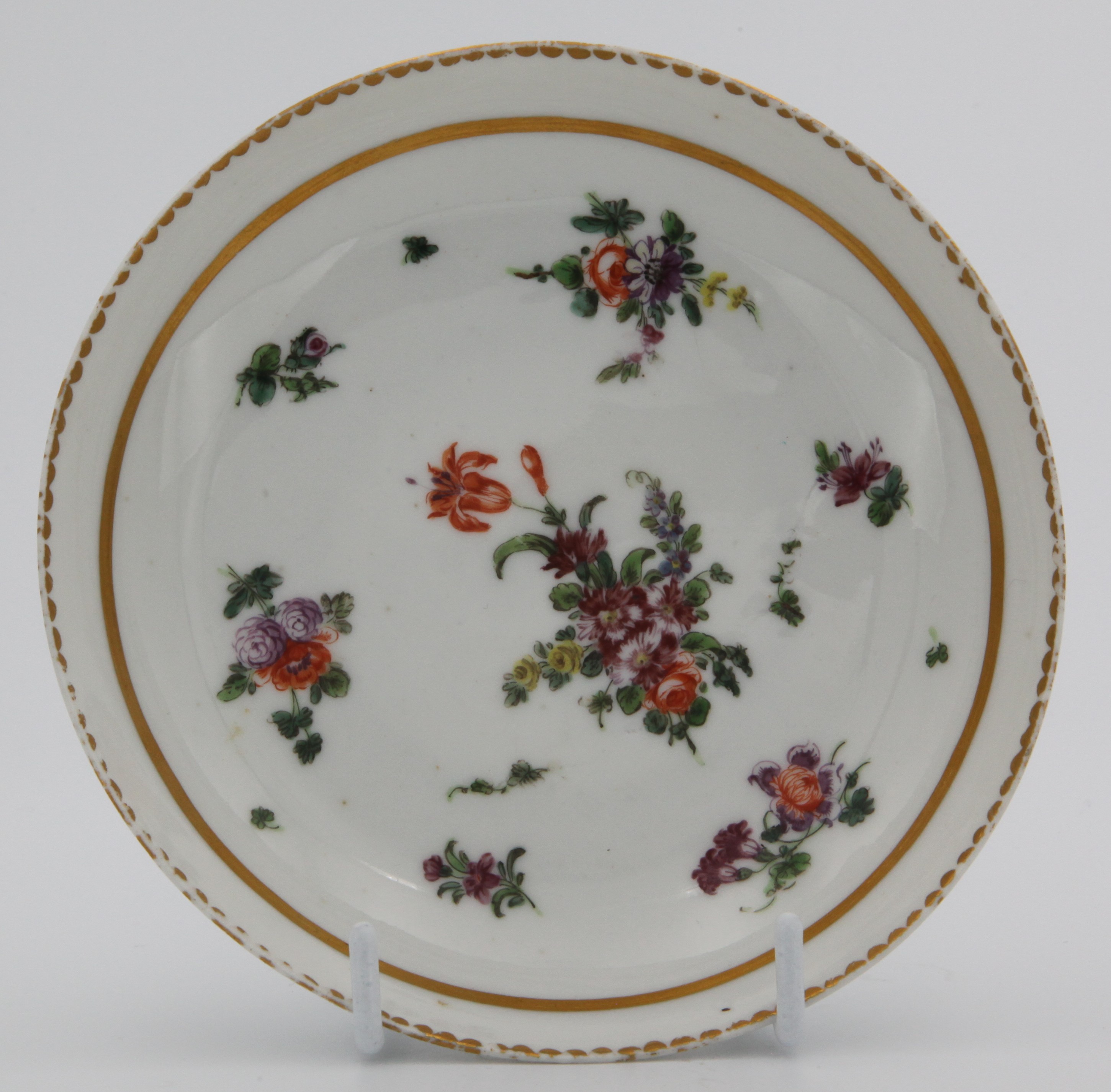 A Bristol coffee saucer  painted with a central spray and scattered sprigs and two gilt borders c. 1773-75.  Mark: none.