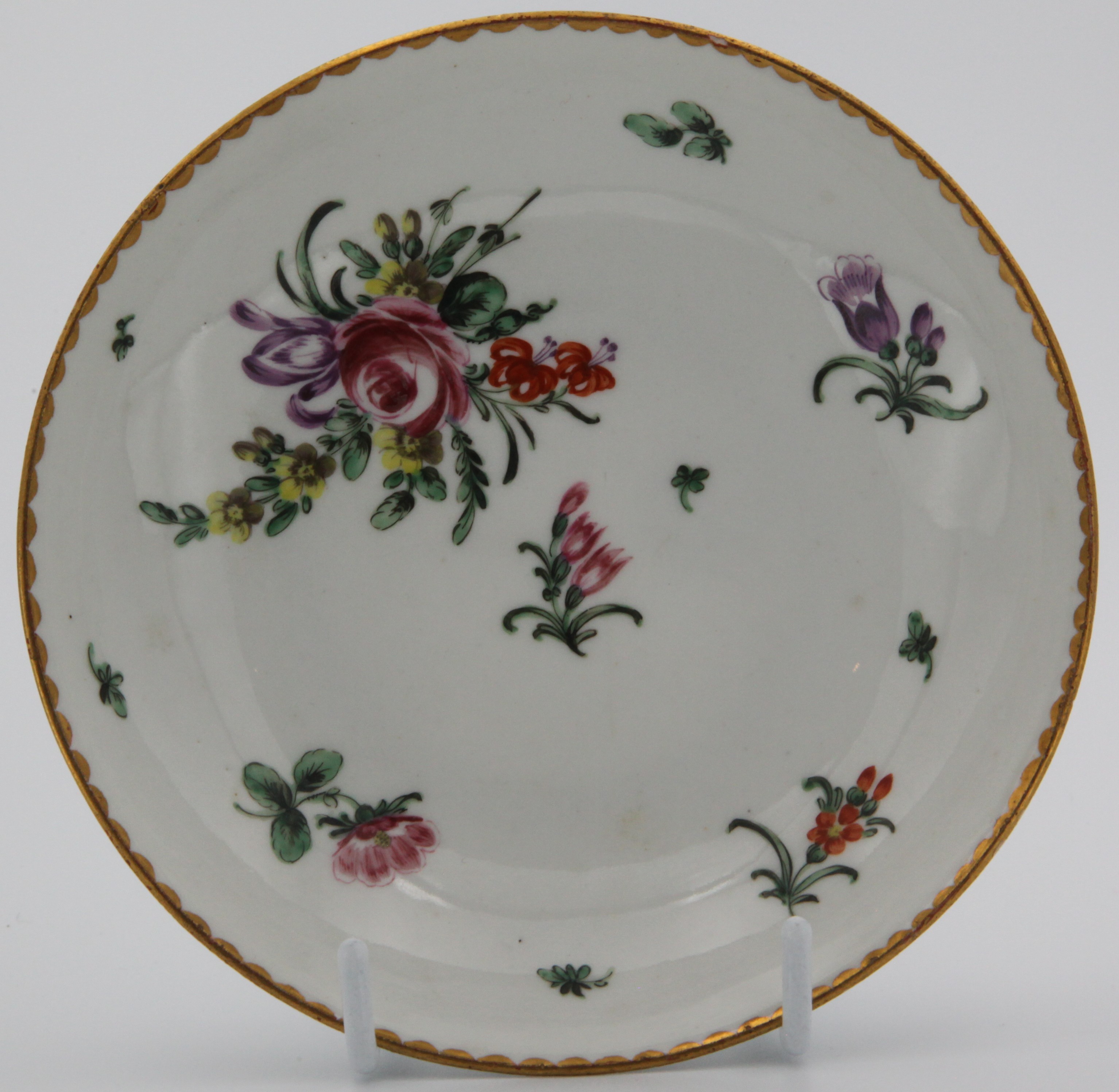 A Bristol saucer painted with a large spray and scattered sprigs under a dentil border c. 1775-78 Mark: X