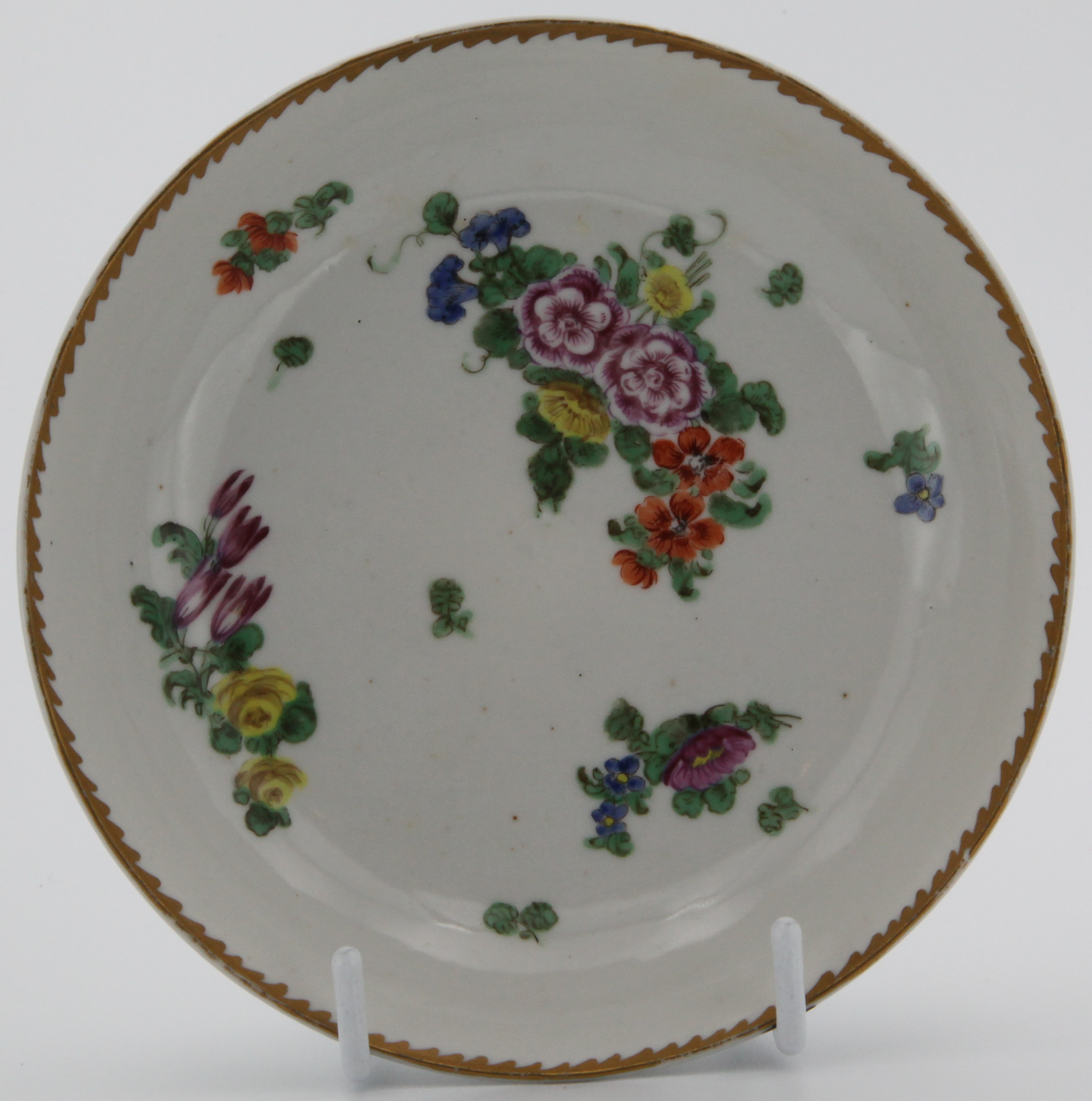 A Bristol saucer painted with a large  spray and scattered sprigs under an angular gilt dentil border c. 1773-75 Mark: none.