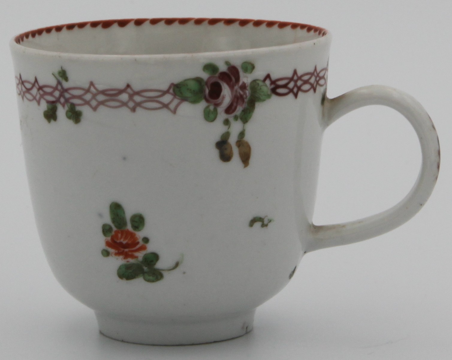 A Bristol coffee cup with simple handle painted with scattered flowers, under a pink chain band suspending flowers and leaves, orange angular dentil rim inside c. 1775-78. No mark