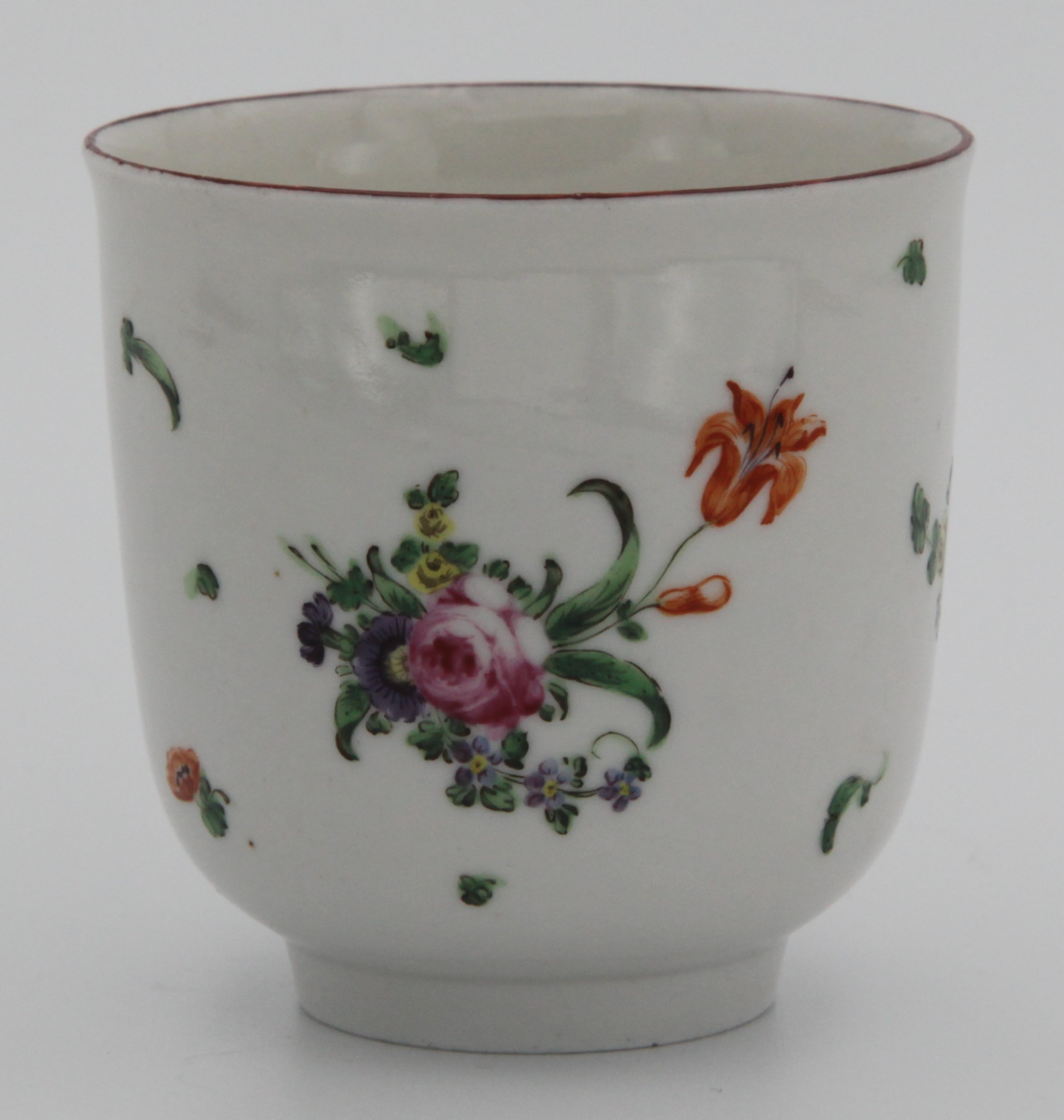 A Bristol coffee cup with plain handle decorated in puce,  painted in enamels with scattered pink, a prominent orange flower and leaves and iron red rim. c. 1775-78. Mark: none.