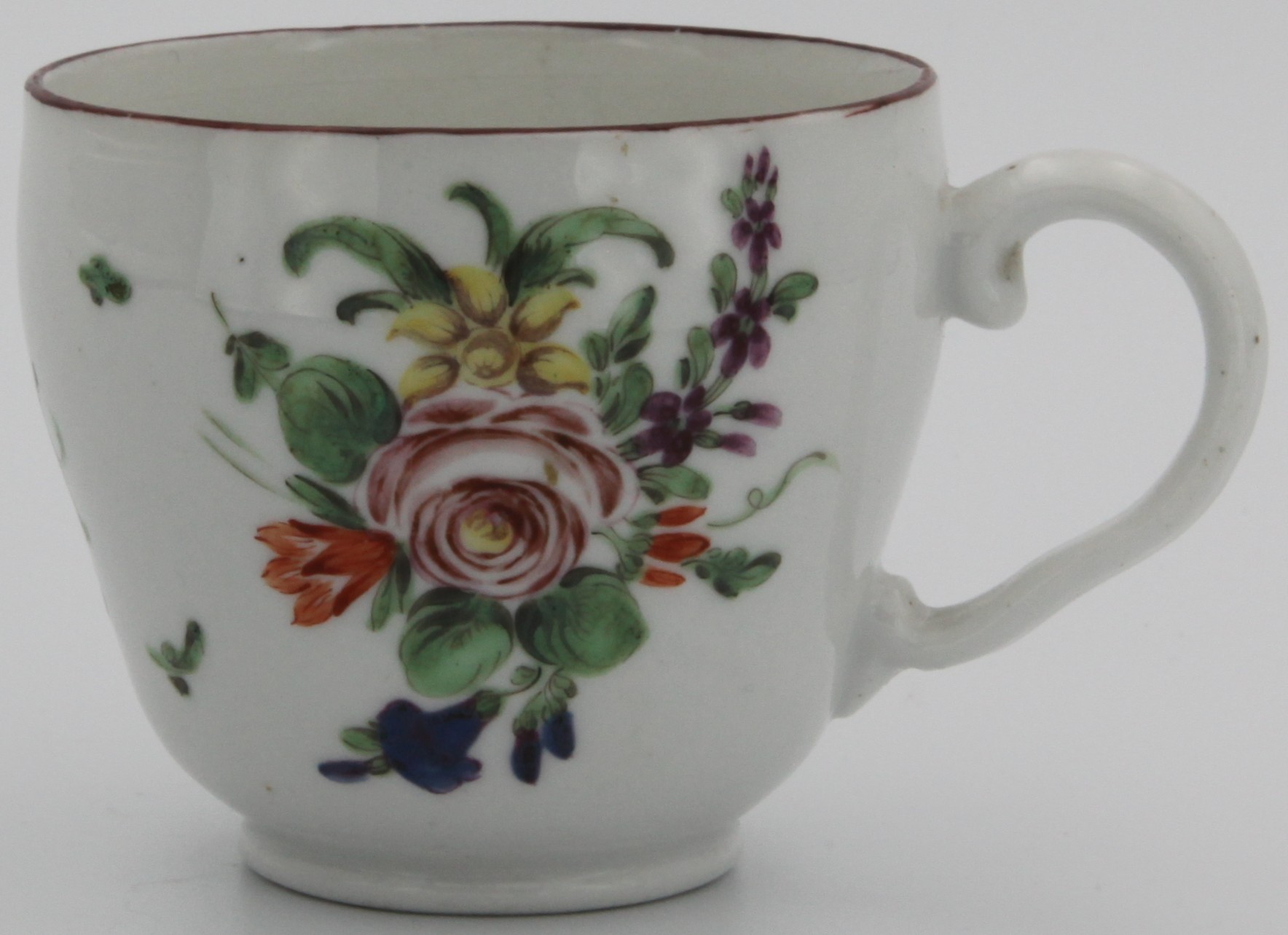 A Bristol coffee cup of ogee form and with ear-shaped handle,  painted with spray of flowers with central rose and scattered flowers and leaves with iron red rim c. 1775-78. Mark: underglaze blue crossed swords with dot and painted blue X.