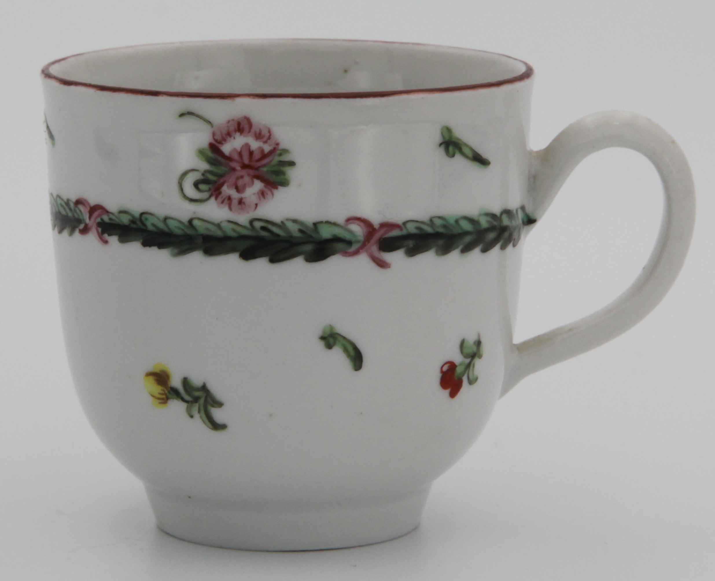 A Bristol coffee cup with simple, undecorated and slightly wonky handle, painted with an acanthus leaf border, scattered flowers and leaves and an iron red rim c. 1775-78. Mark: none.