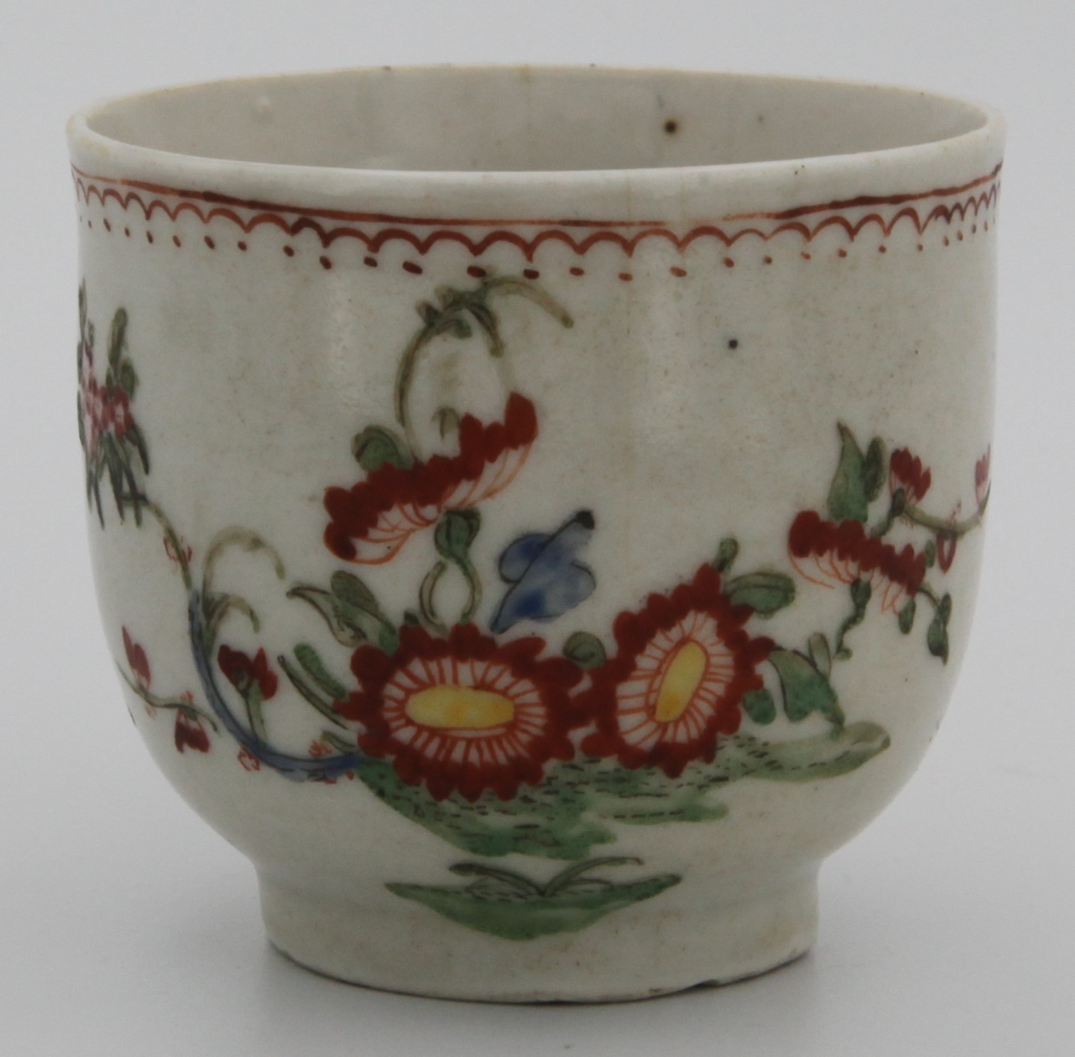 A Plymouth hard paste porcelain coffee cup, hand painted with a floral pattern under thin orange stylized band. c1768-70.  Remnants of a mark (orange tin?).