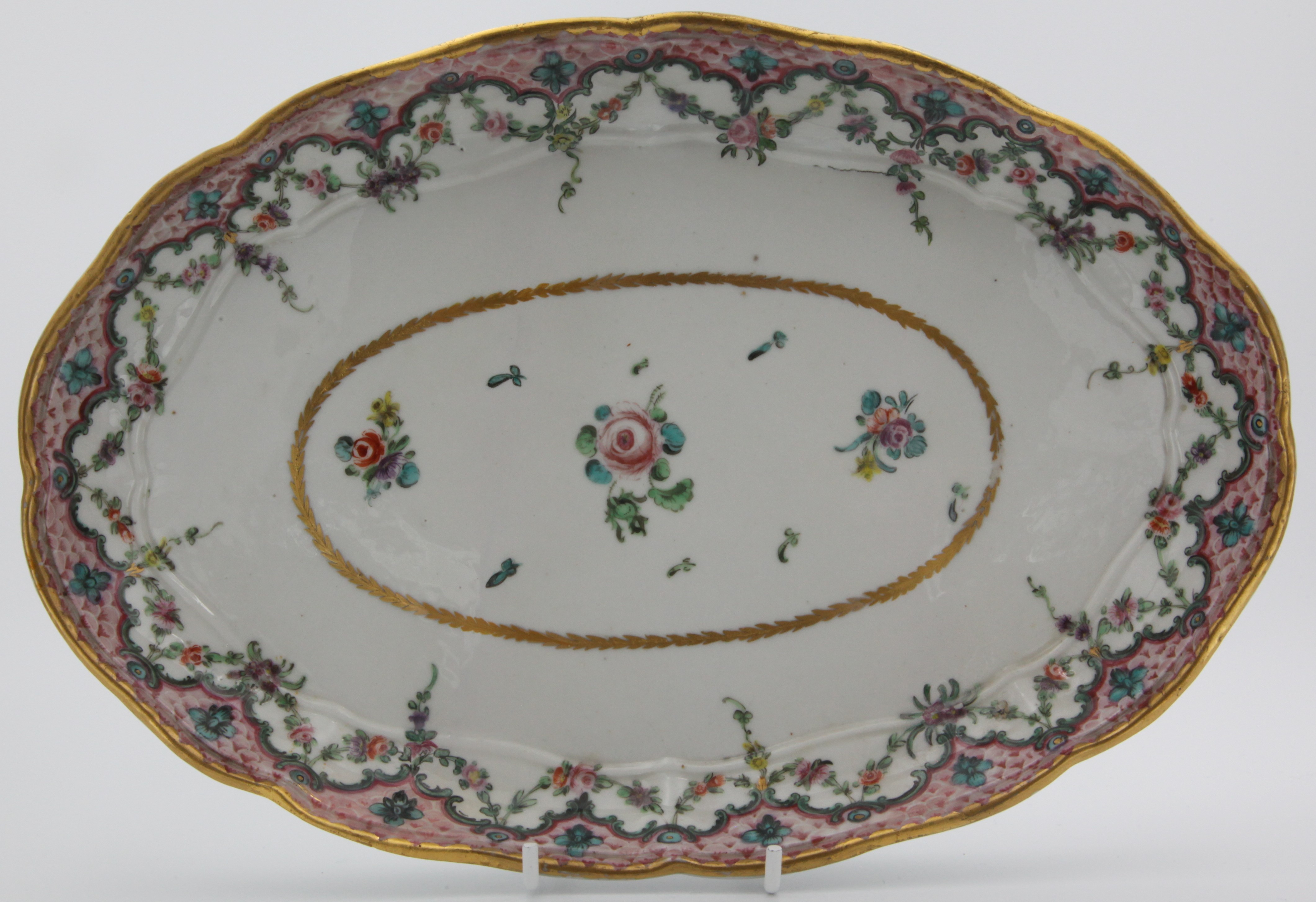 An oval tray from a rare Bristol cabaret set,  painted in coloured enamels with scattered flowers, within a pink scale border, with green ‘C’ scrolls and flower heads, suspending garlands of flowers and leaves,  circa 1775.