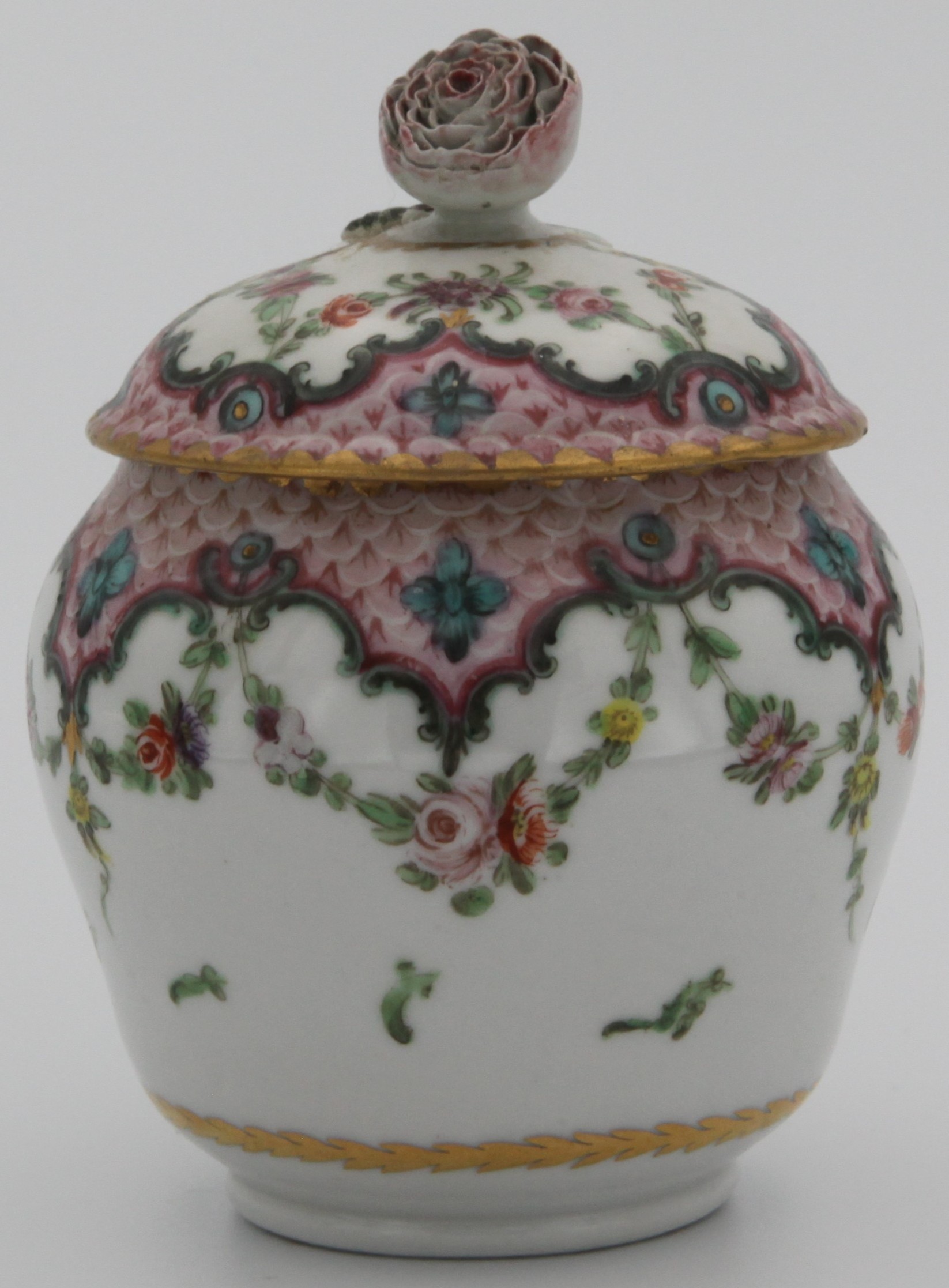 An ovoid sucrier and lid with flower knop, from a rare Bristol cabaret set,  painted in coloured enamels with scattered flowers, within a pink scale border, with green ‘C’ scrolls and flower heads, suspending garlands of flowers and leaves,  circa 1775,  underglaze blue crossed swords and dot marks.