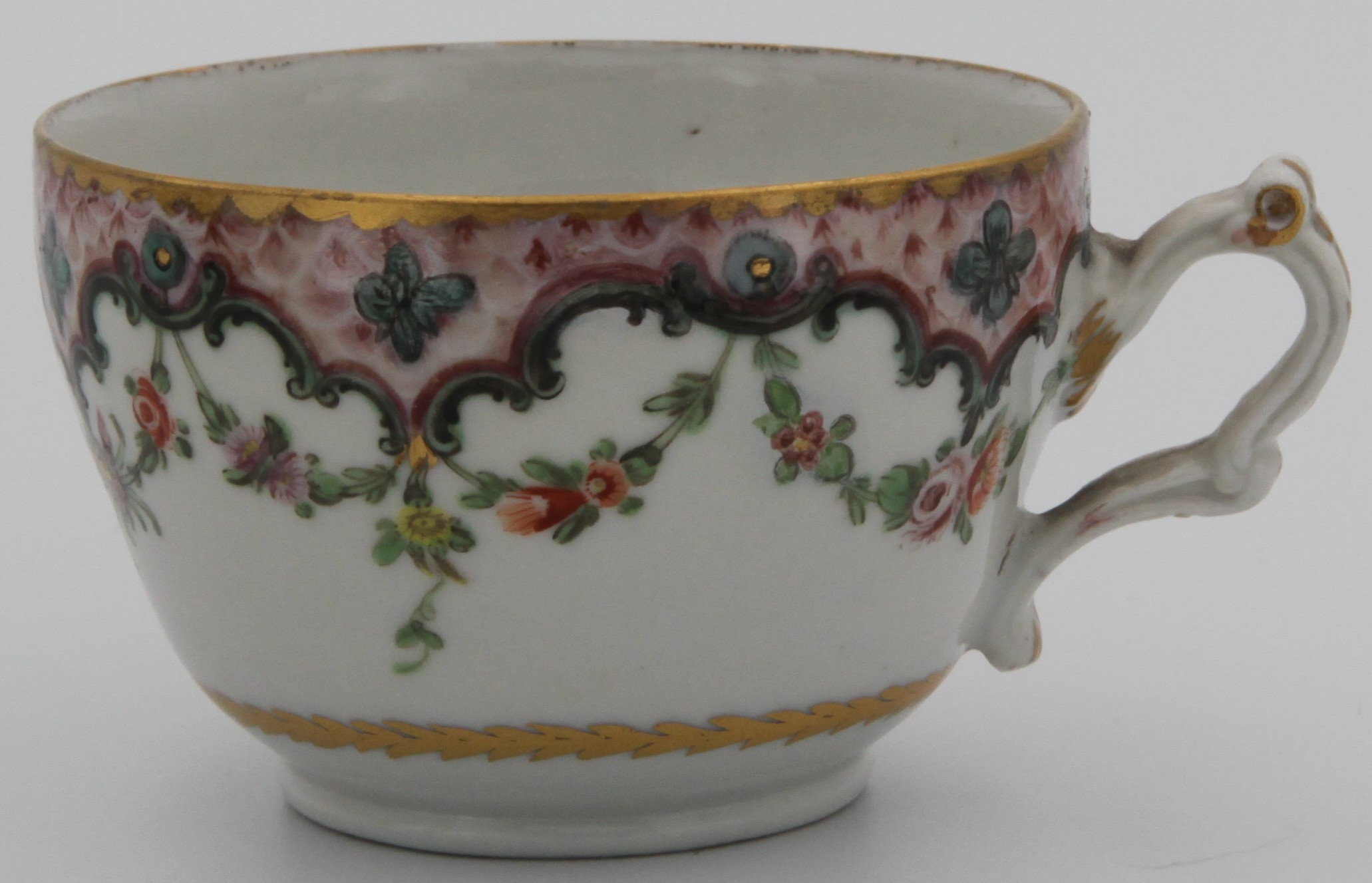 A tea cup  from a rare Bristol cabaret set, the cup with double ‘C’ scroll handle,  painted in coloured enamels with scattered flowers, within a pink scale border, with green ‘C’ scrolls and flower heads, suspending garlands of flowers and leaves,  circa 1775.