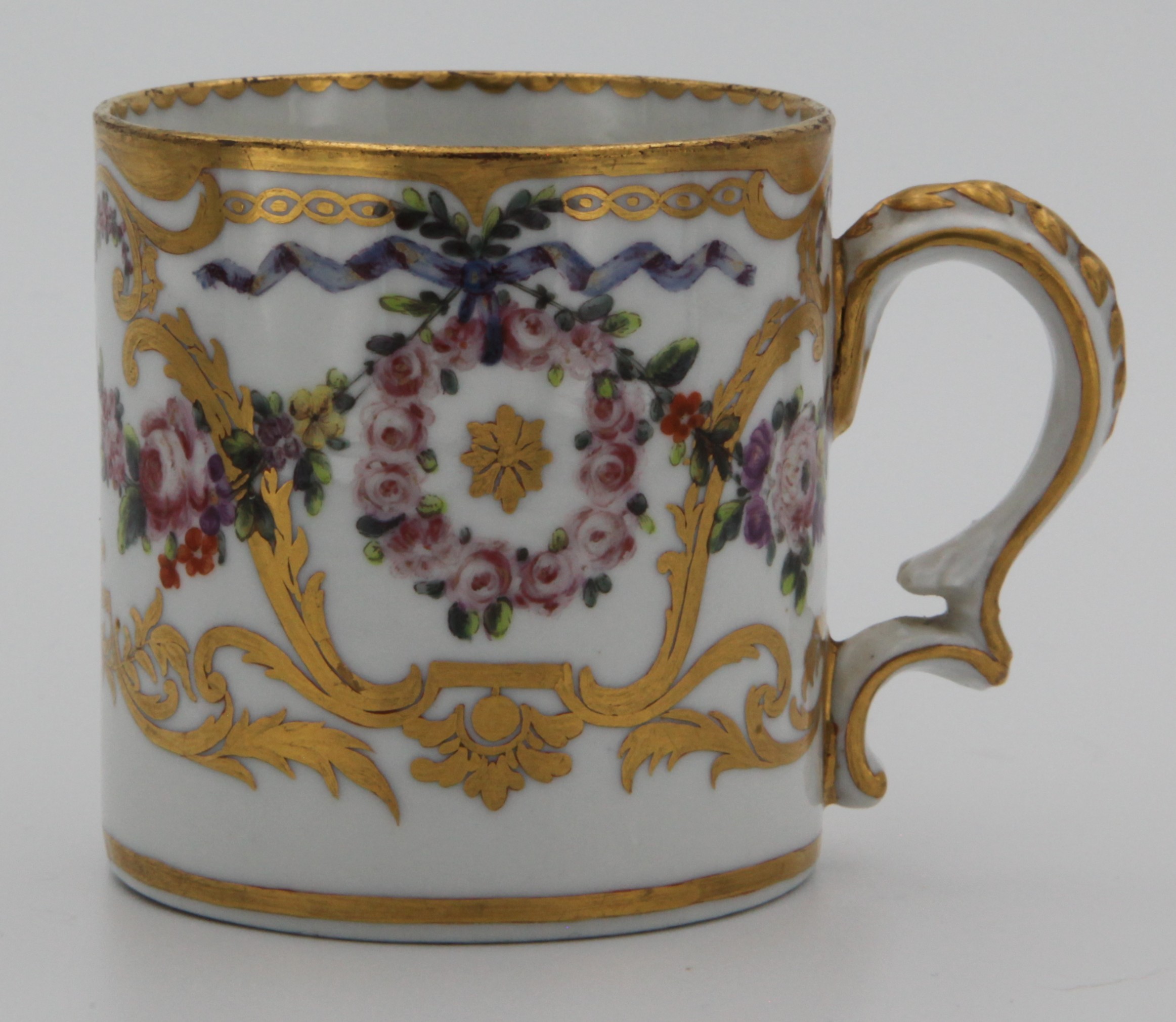 An extremely fine Bristol cylindrical cabinet cup with elaborate ‘C ’scroll handle moulded with leaves and husks, superbly painted in coloured enamels with swags of flowers, and roundels of pink roses suspended from blue ribbons, within gilt leaf scrolls,  circa 1775, blue painted X marks and numeral 3. in gilt.