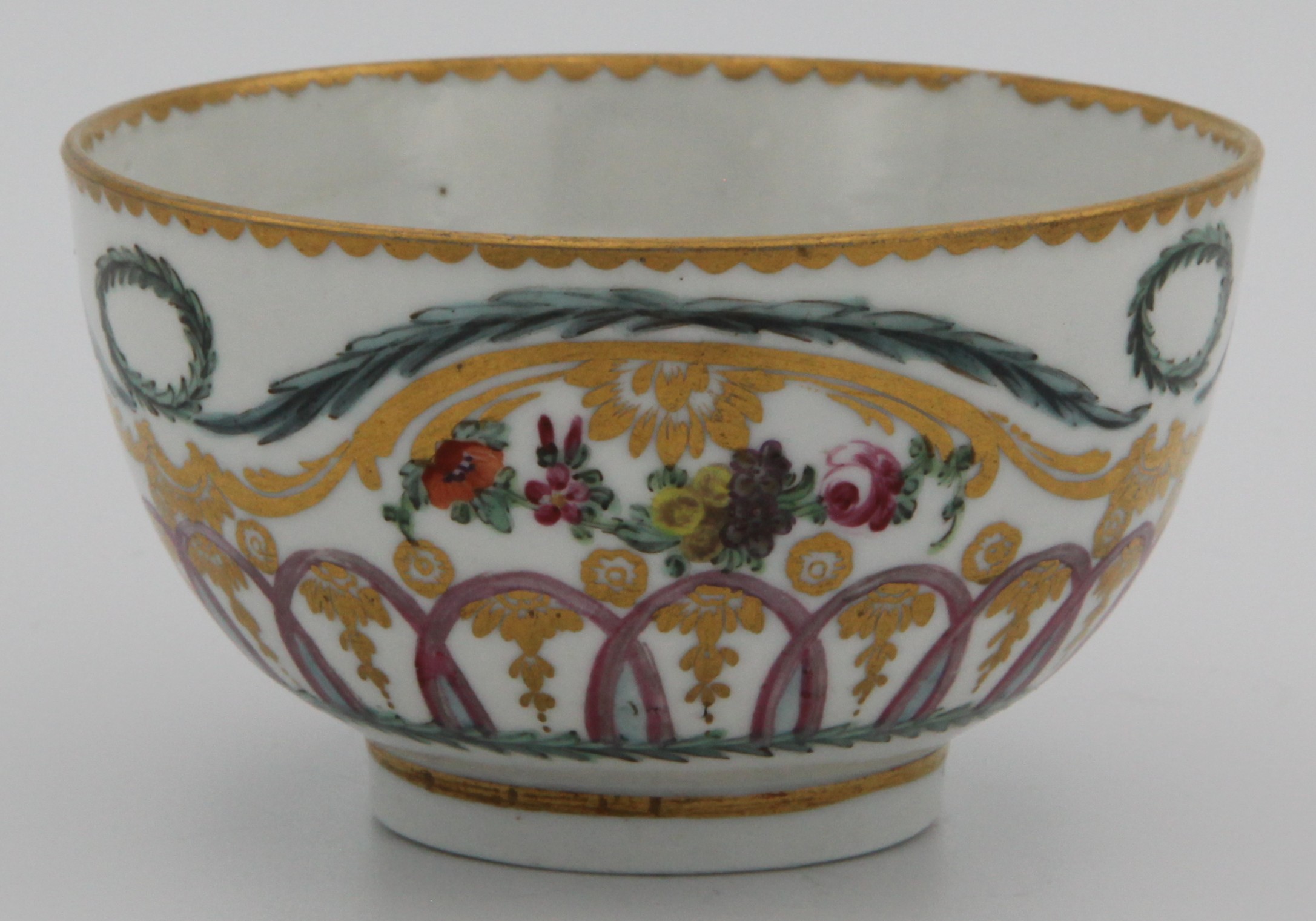 A very fine Bristol tea bowl, painted in coloured enamels with flowers and leaves, within scrolling gilt leaf and green and turquoise laurel bands, with oval laurel garlands, and with a pale blue, puce and gilt interlined band, gilt dentil rims, circa 1775, blue painted crossed swords marks and numeral 2. in gilt