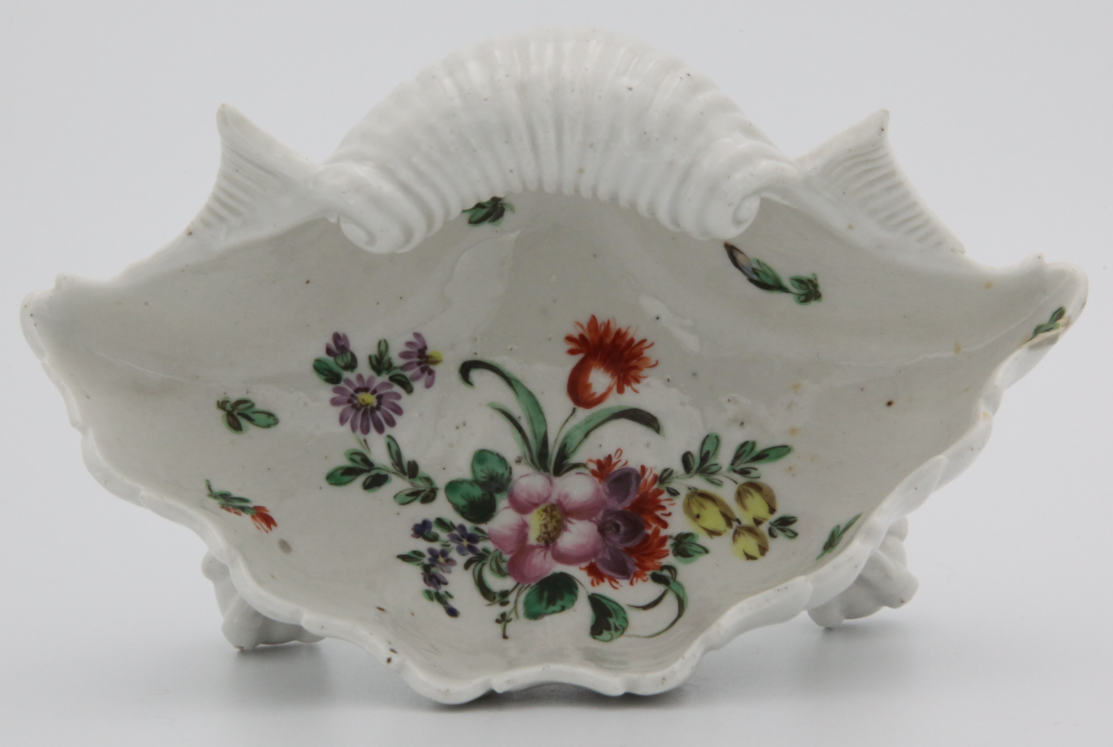 A rare Bristol Porcelain Shell Salt c.1772-1774. Modelled as a shell upturned on 3 claw and ball feet, the interior painted with a spray of flowers. Mark: X6.  A similar Salt is illustrated on page 146 of Nicholas Panes book 'English Potter - American Patriot? - Extracts from the extraordinary life of Richard Champion.' Another example is also in the Merchant Ventures Hall in Bristol where Champion was a member.