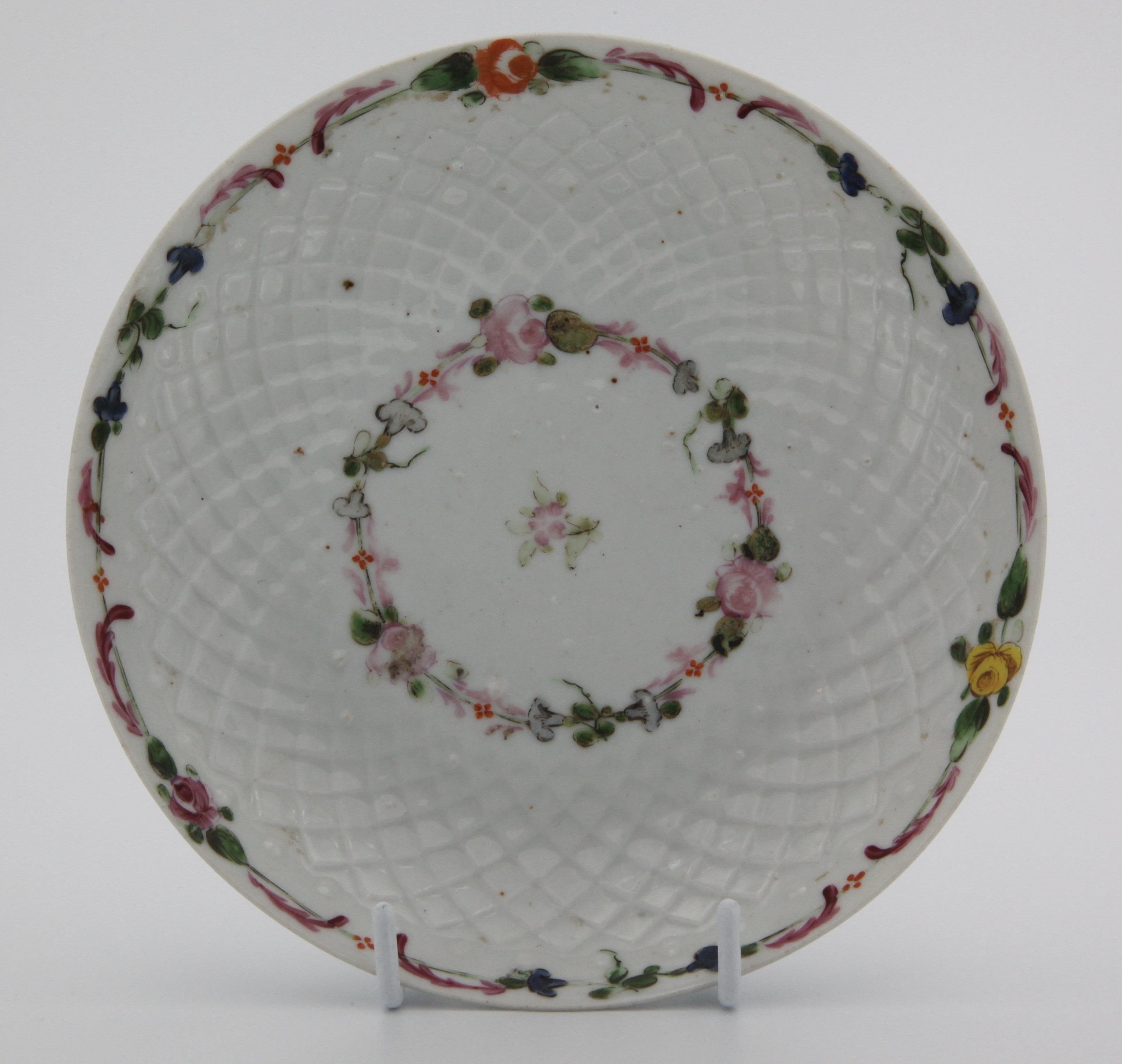A Bristol porcelain pinecone-moulded chocolate cup stand, painted with pink and green floral garland encirling central sprig, a garland of couloured flowers and leaves around the rim. No mark c.1774