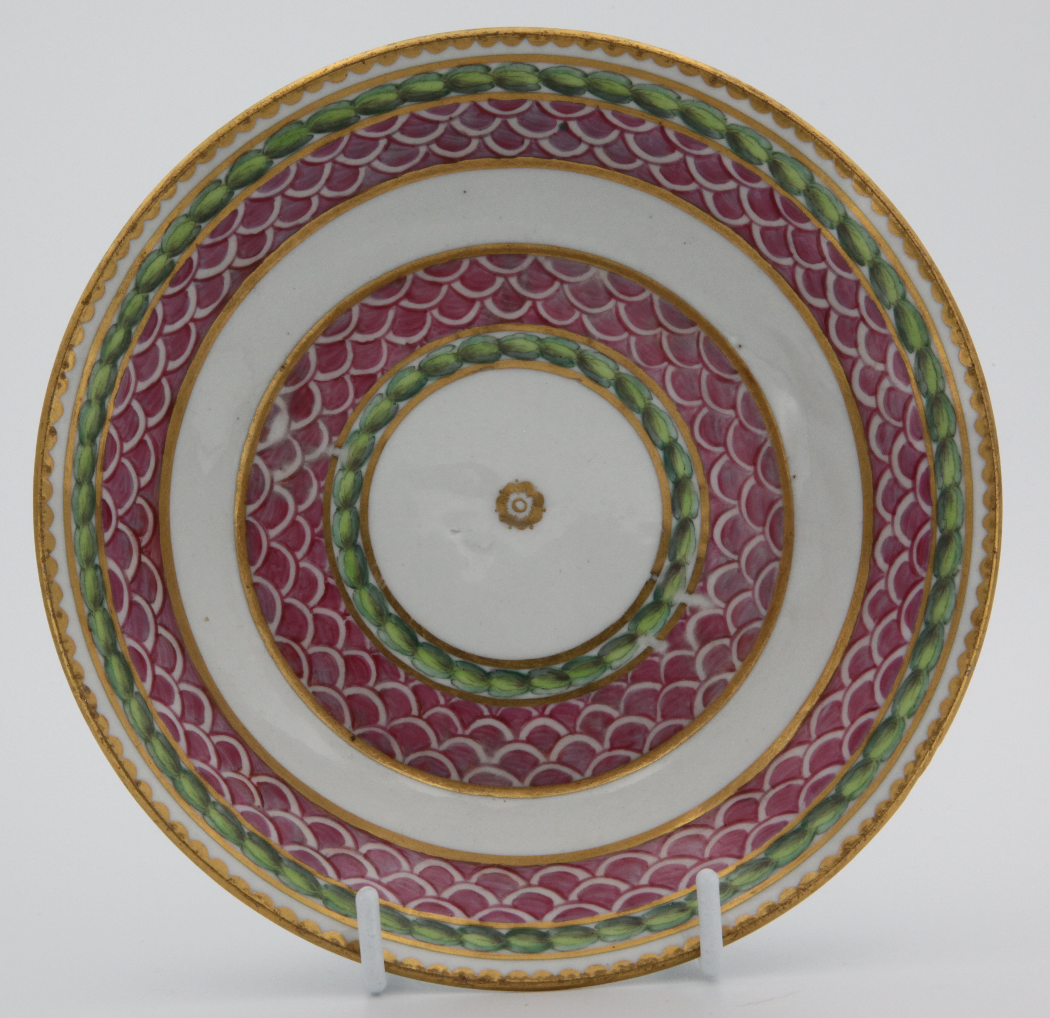 A fine Bristol coffee saucer, painted in pink with scale bands, within green laurel borders, gilt dentil rims, circa 1775, blue painted  X4 on saucer.  See Albert Amor Limited, The Alfred Trapnell Collection, 1912, numbers 27 and 28 for similar examples