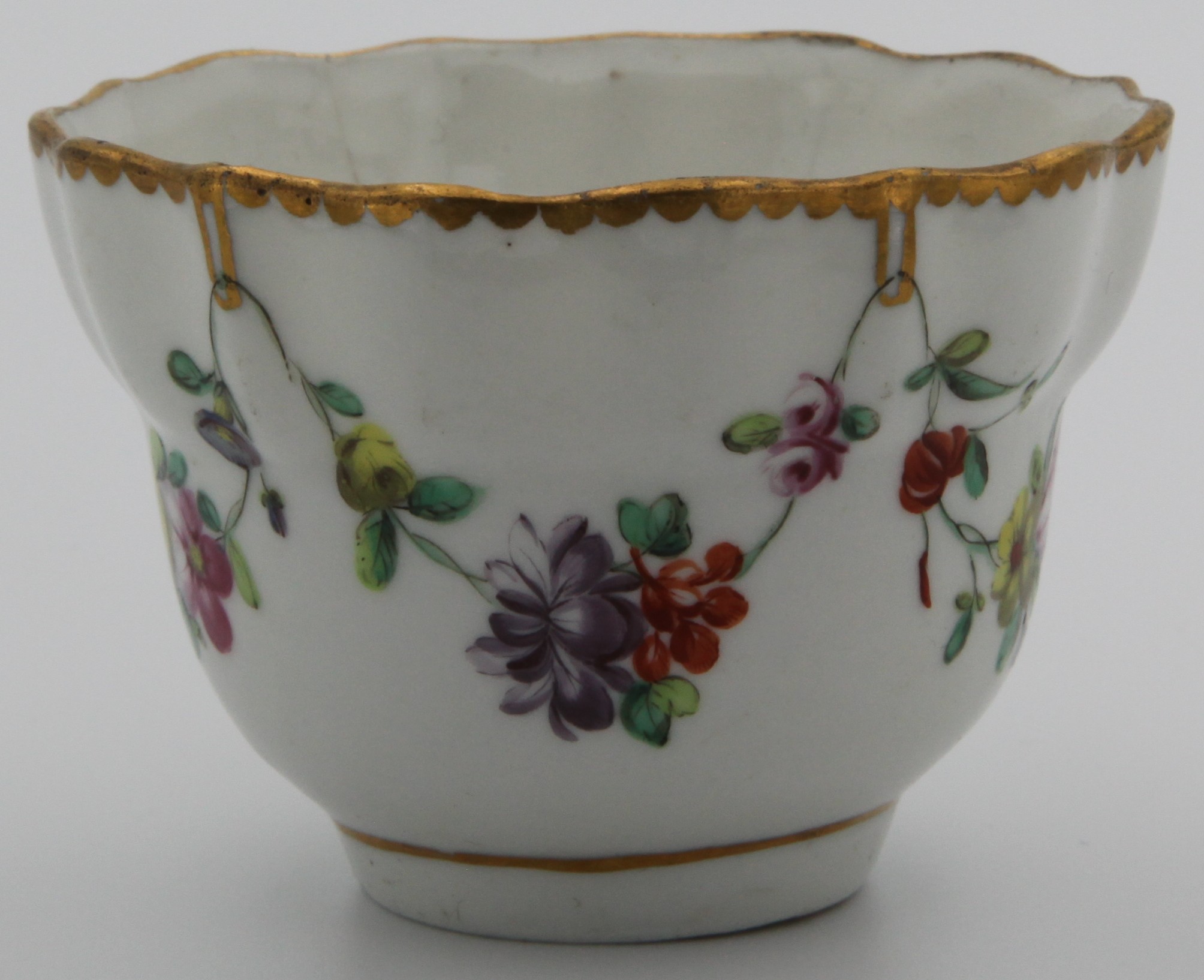 Bristol ogee teabowl painted with chains of flowers hanging from gold loops suspended from a heavy gilt dentil rim, a flower in the bottom of the bowl. Mark: faint Xb