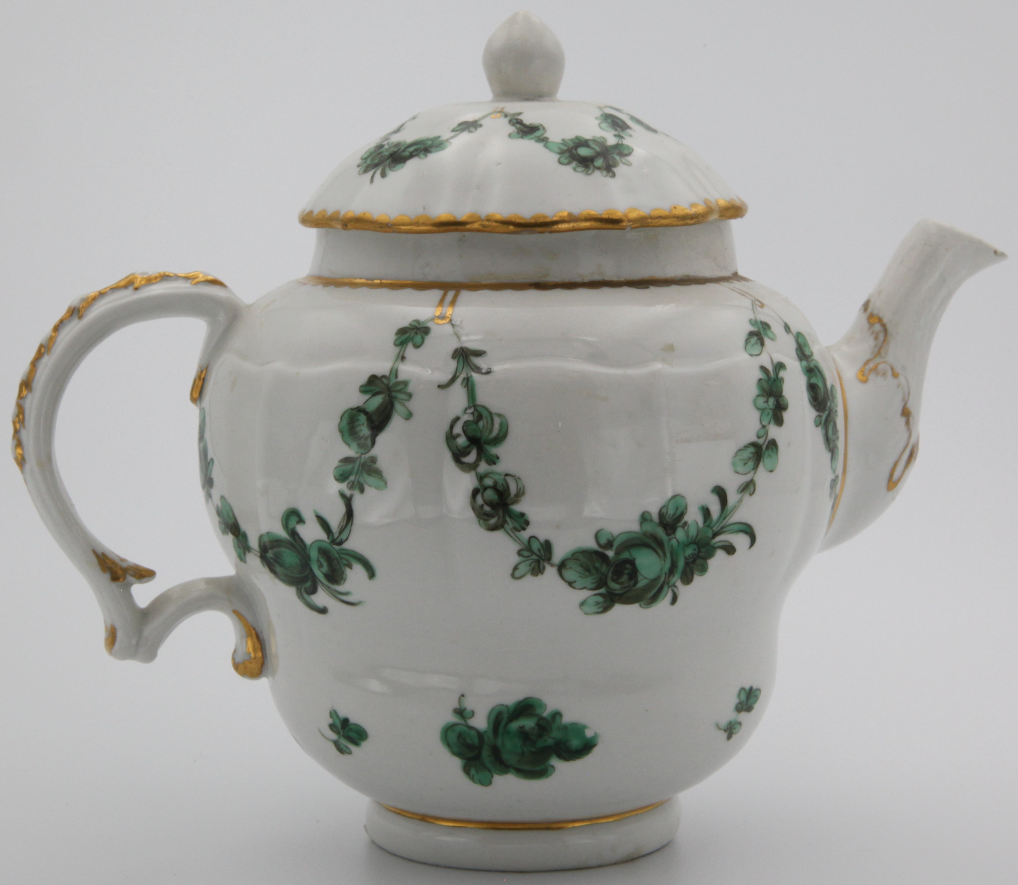 Bristol ogee-shaped waisted teapot and cover, with moulded and gilt-decorateds scroll handle, finely painted  with green swags of flowers suspended from gilt loops hanging from heavy gilt dentil rim. Mark:  Blue X