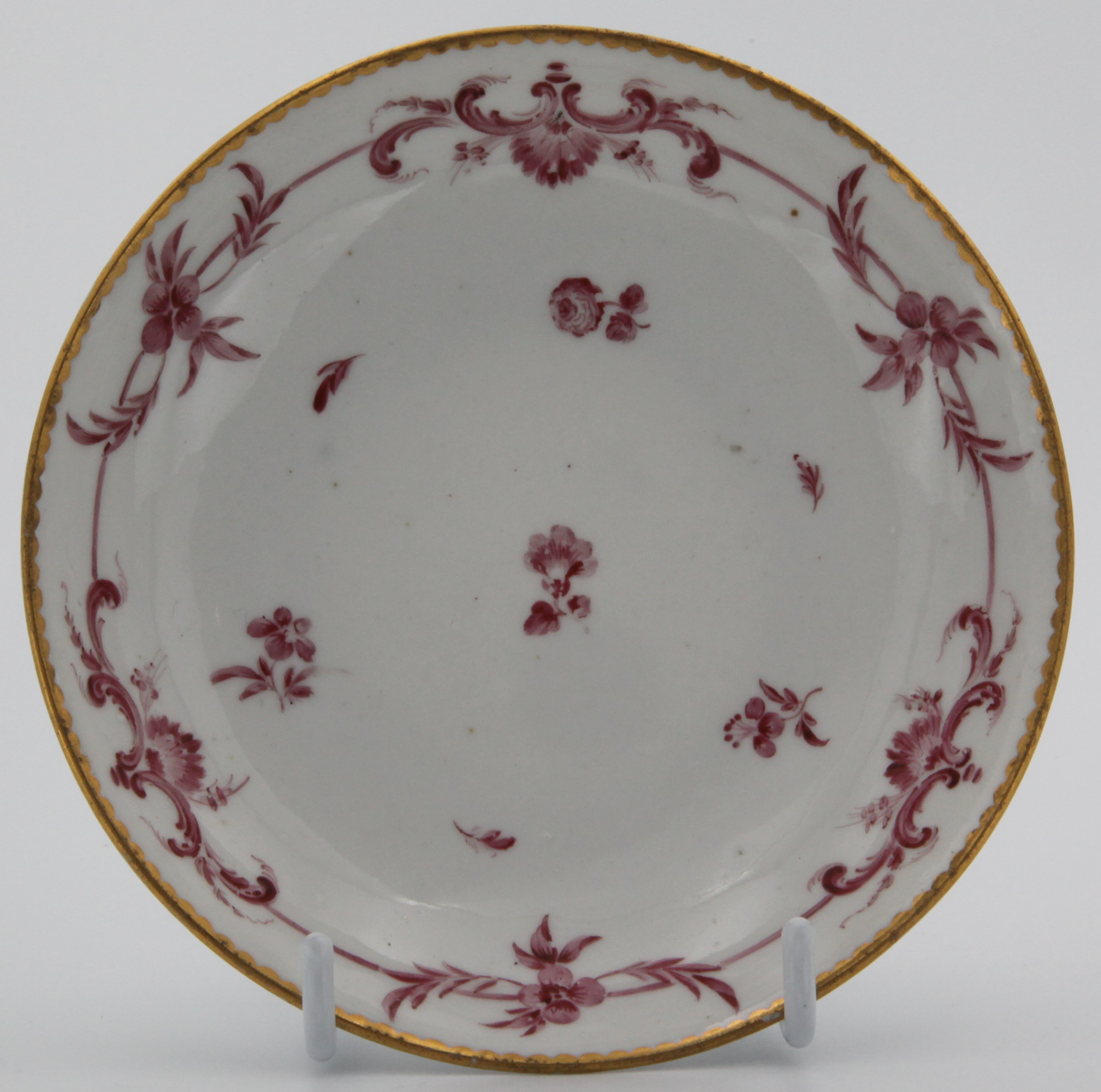 A fine Bristol saucer painted with monochrome puce scroll band with scattered flowers under gilt dentil rim. Mark: dark blue crossed swords and gilt 6.